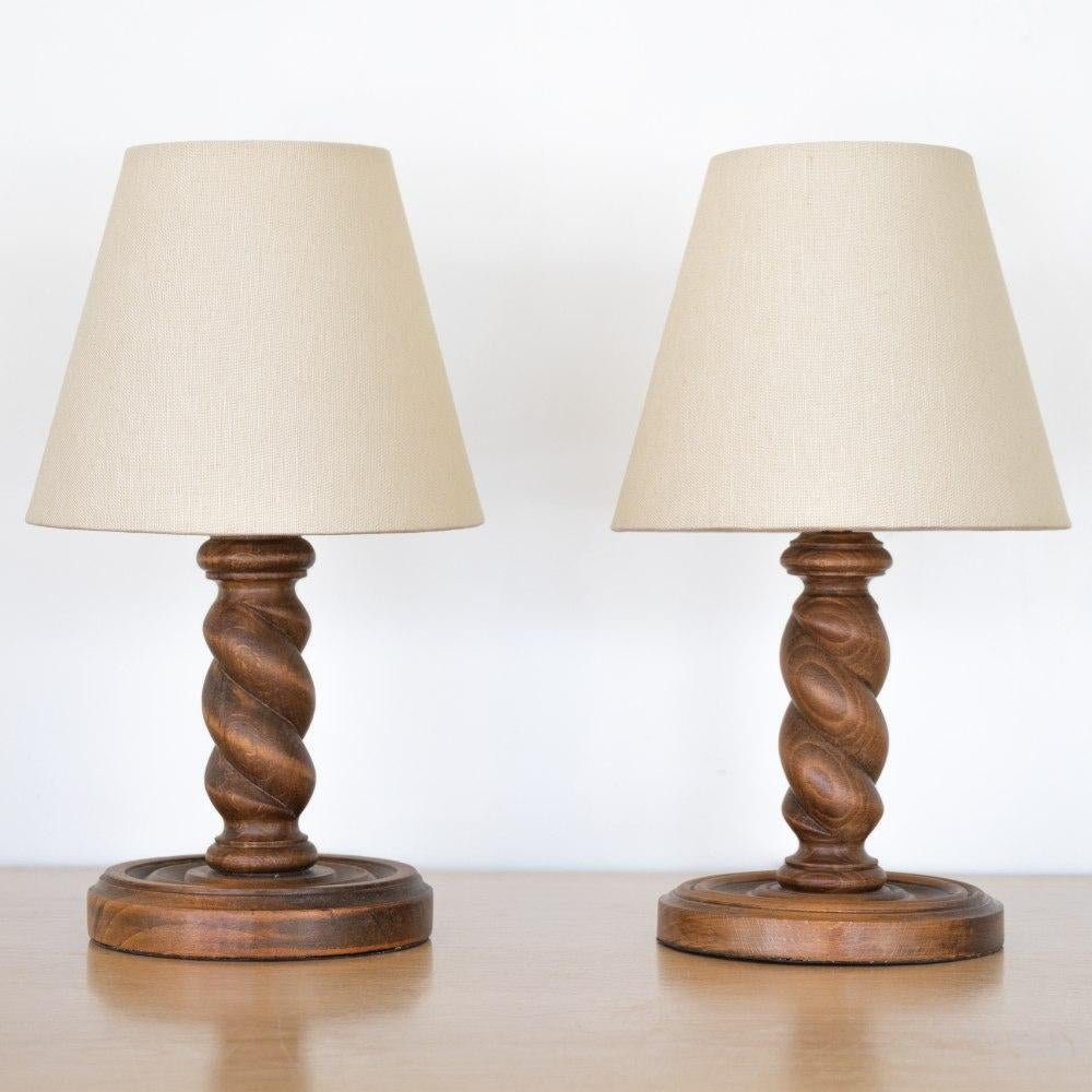 Beautiful petite pair of 1940's carved wood table lamps from France. Twisted wood stems with original wood finish and circular base. New creamy linen tapered shades and newly re-wired. Sold and priced as a pair. Each takes one E12 base bulb, 25 W or