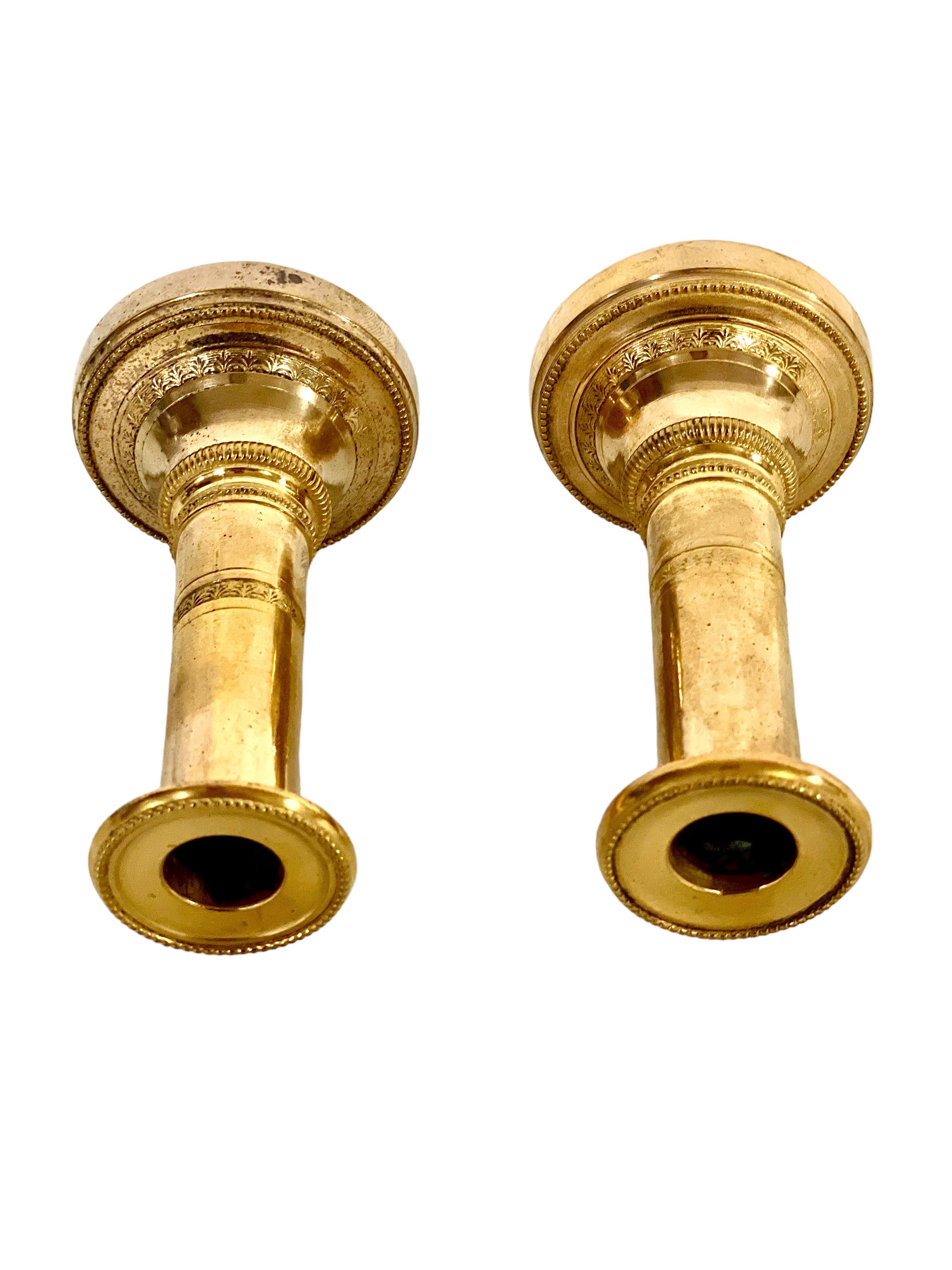 Ein feines Paar vergoldeter Bronze-Kerzenhalter aus dem 19. Jahrhundert in einem einfachen, aber eleganten Design. Mit einer Höhe von ca. 10 cm ruht jeder dieser zierlichen Kerzenhalter auf einem runden Sockel, der mit einem klaren und einfachen
