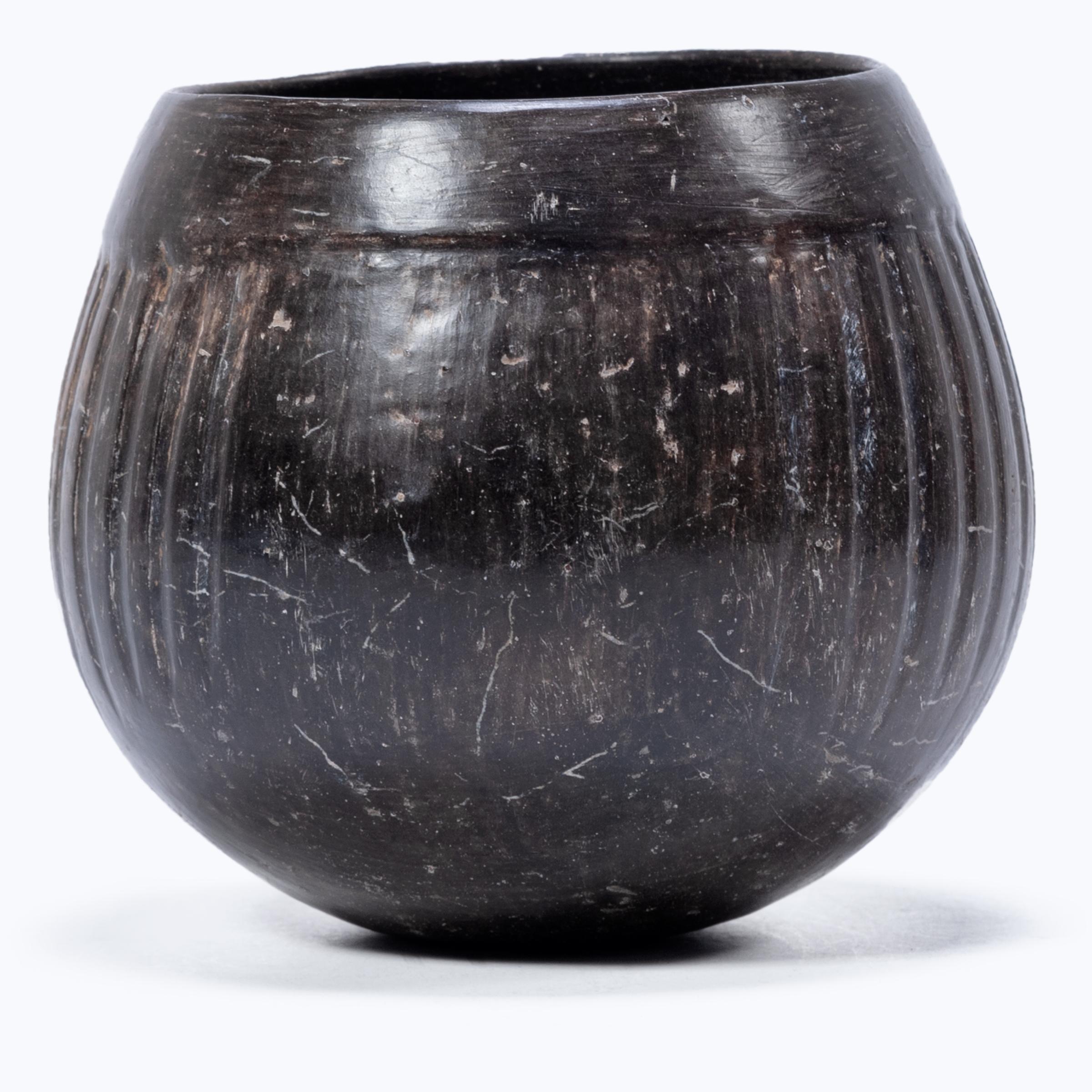 Exhibiting a rich patina, this petite blackware vessel shows many telltale signs of Pre-Columbian pottery. The darkened surface was achieved by applying a mineral-rich slip for a monochrome finish that designates the vessel as an everyday object.