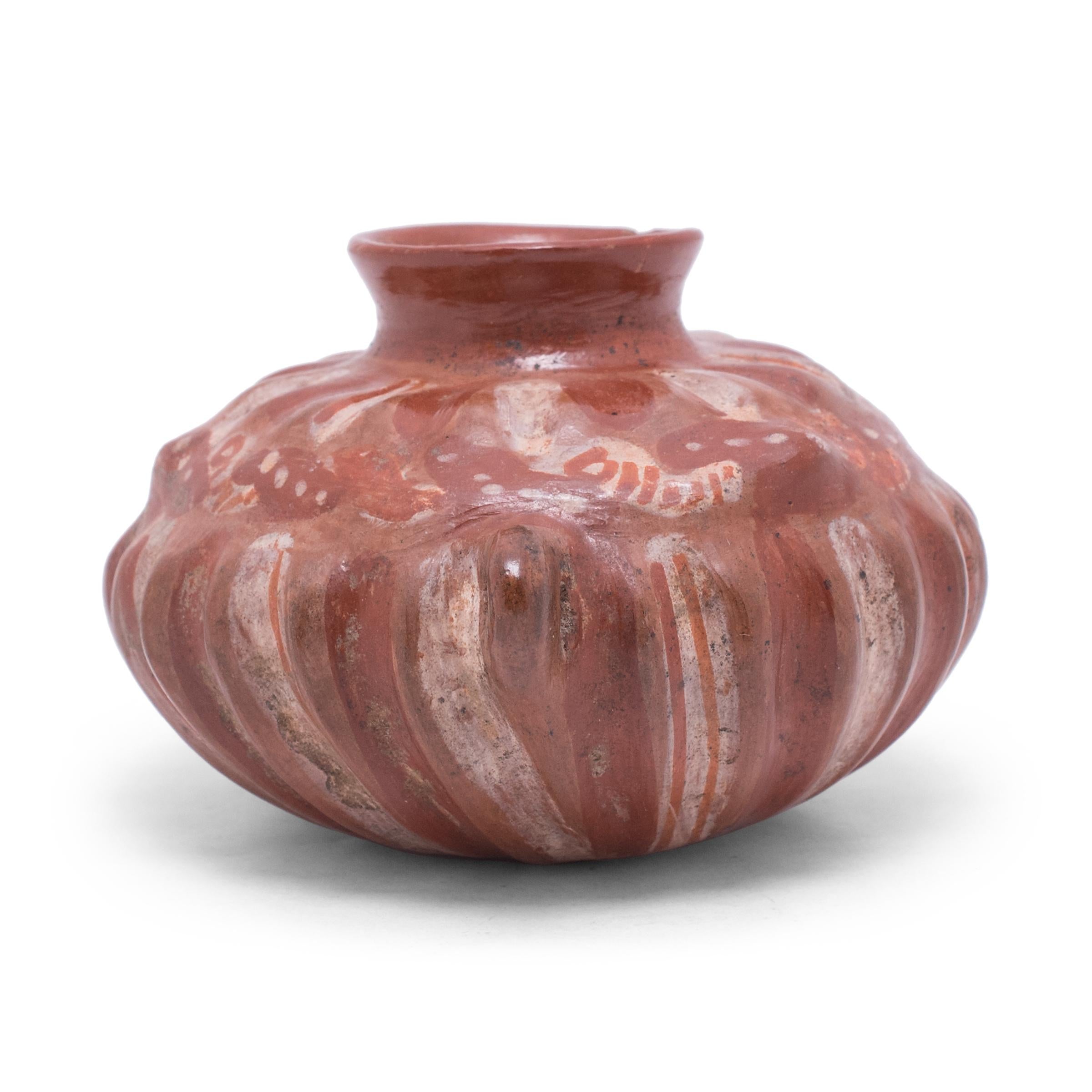 This small olla jar is a beautiful example of Mesoamerican pottery, decorated with red, white, and orange slip in the style of Chupícuaro ware. The wide, globular body of the vessel has a lobed shape resembling a squash or cactus, accentuated by