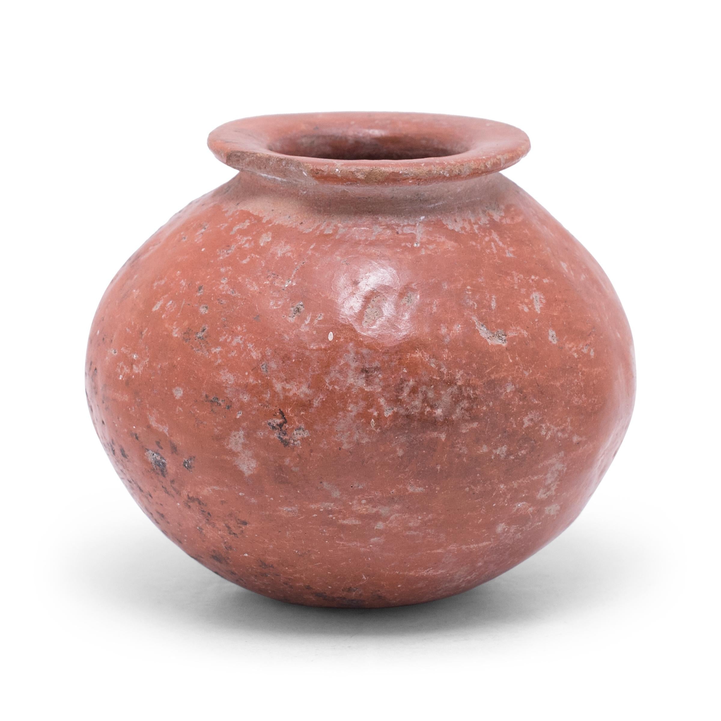 Exhibiting a rich patina and a beautifully irregular pattern of pitted wear, this petite redware olla vessel shows many telltale signs of Pre-Columbian pottery. The vessel has a globular form with a rounded base, constricted neck, and flattened rim.