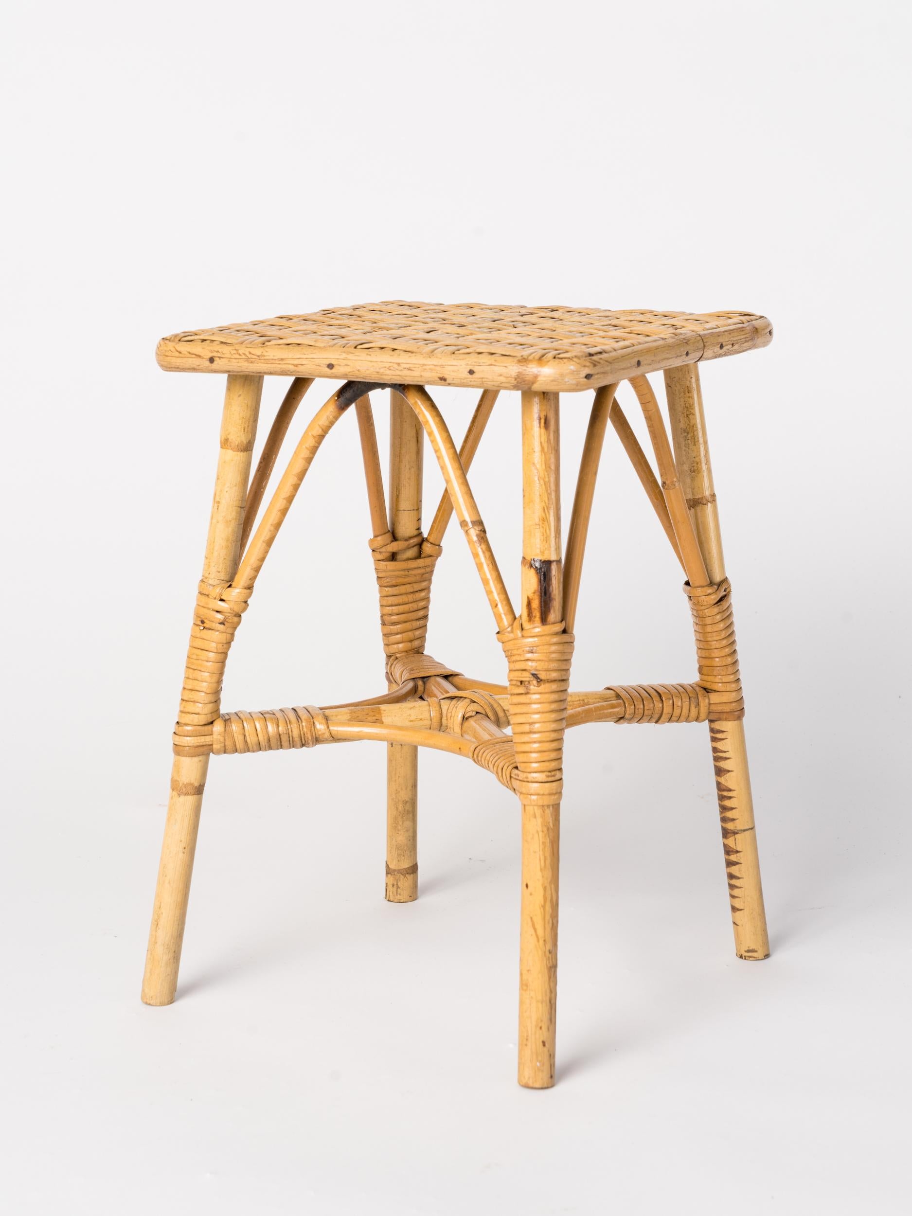 Four legged petite rattan low stool. In the style of Louis Sognot. Good vintage condition. This item will ship from France and can be returned to either France or to a Long Island City location. 
 