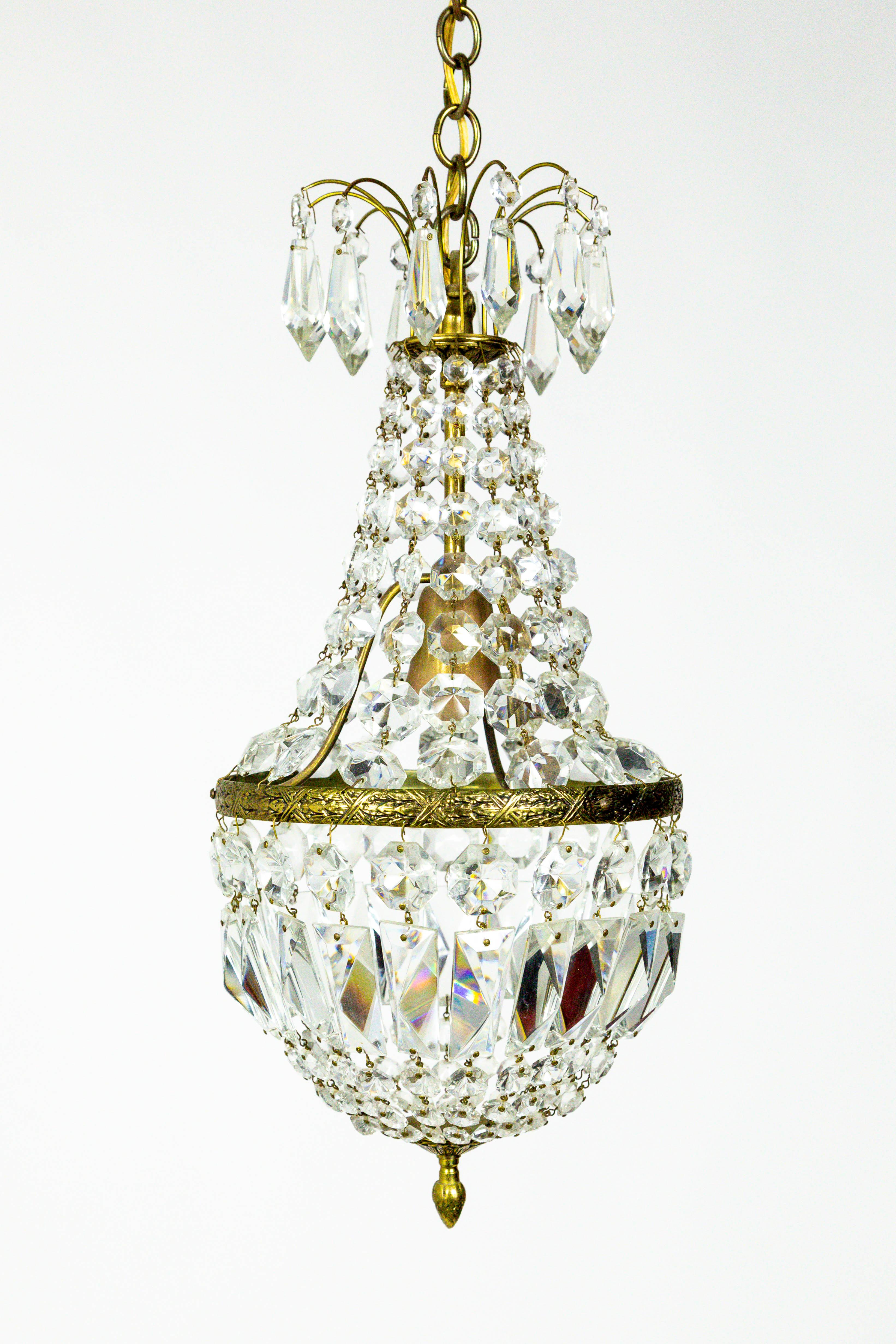 A lovely, small, crystal Regency style, basket chandelier made in the 1970s. Detailed with a decorative, brass band and acorn finial, and faceted drop, baguette, and bead crystals. American. 20