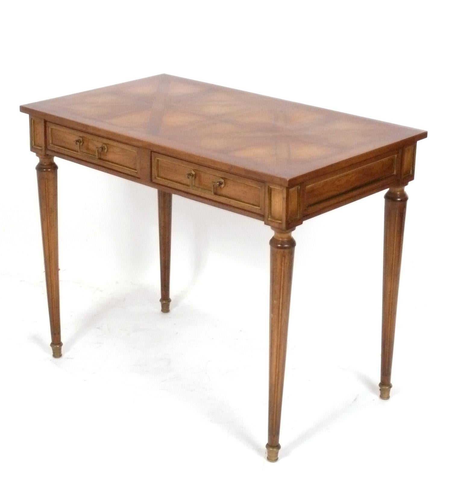 Petite Regency Style Desk or Console Table, French style but probably American, circa 1950s. It is a versatile size and can be used as a desk, vanity, console table, or bar. It features an elegant inlaid parquet top and brass hardware which retains