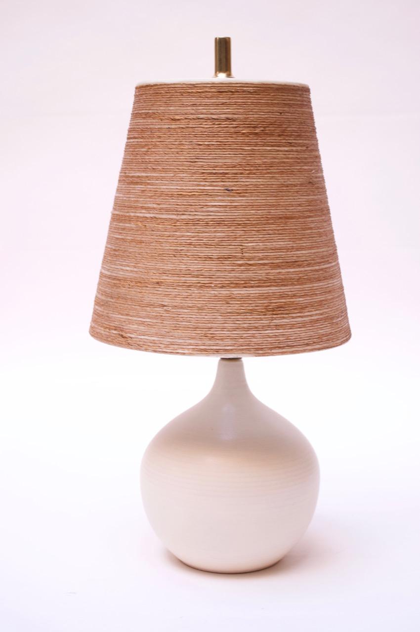 This small scale orb-shaped table lamp was designed and manufactured in the 1960s by Lotte and Gunnar Bostlund after they relocated their ceramic studio from Denmark to Canada. Includes Lotte jute shade, as shown. 
The applied, unpolished brass