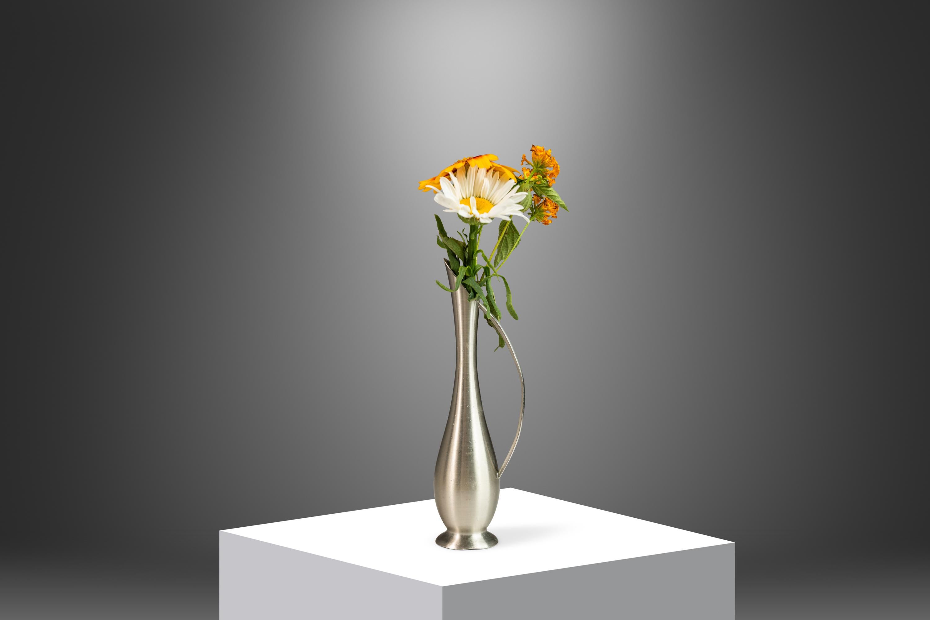 This delicate sculptural vase by Metawa exemplifies the modernist elegance of mid-century design from the 1960s. Crafted in Holland from solid pewter, the piece features a slender, elongated form with a gracefully curved handle and a subtly flared