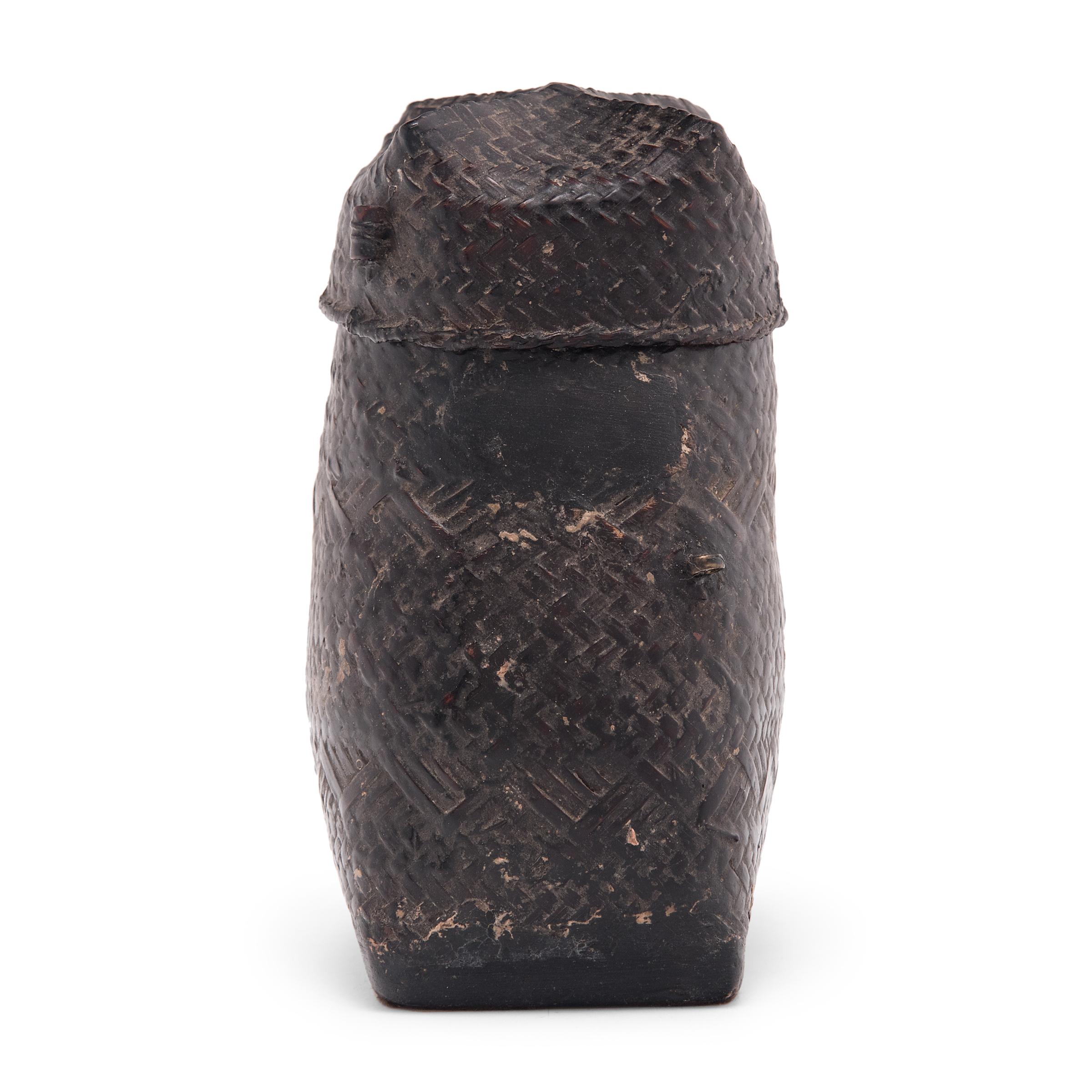Dated to the early 20th-century, this petite box was woven of thin bamboo strips and coated in a putty-like substance known as thayo, comprised of black lacquer and sawdust. The box has a square wooden base and tapers to a narrow rounded opening.