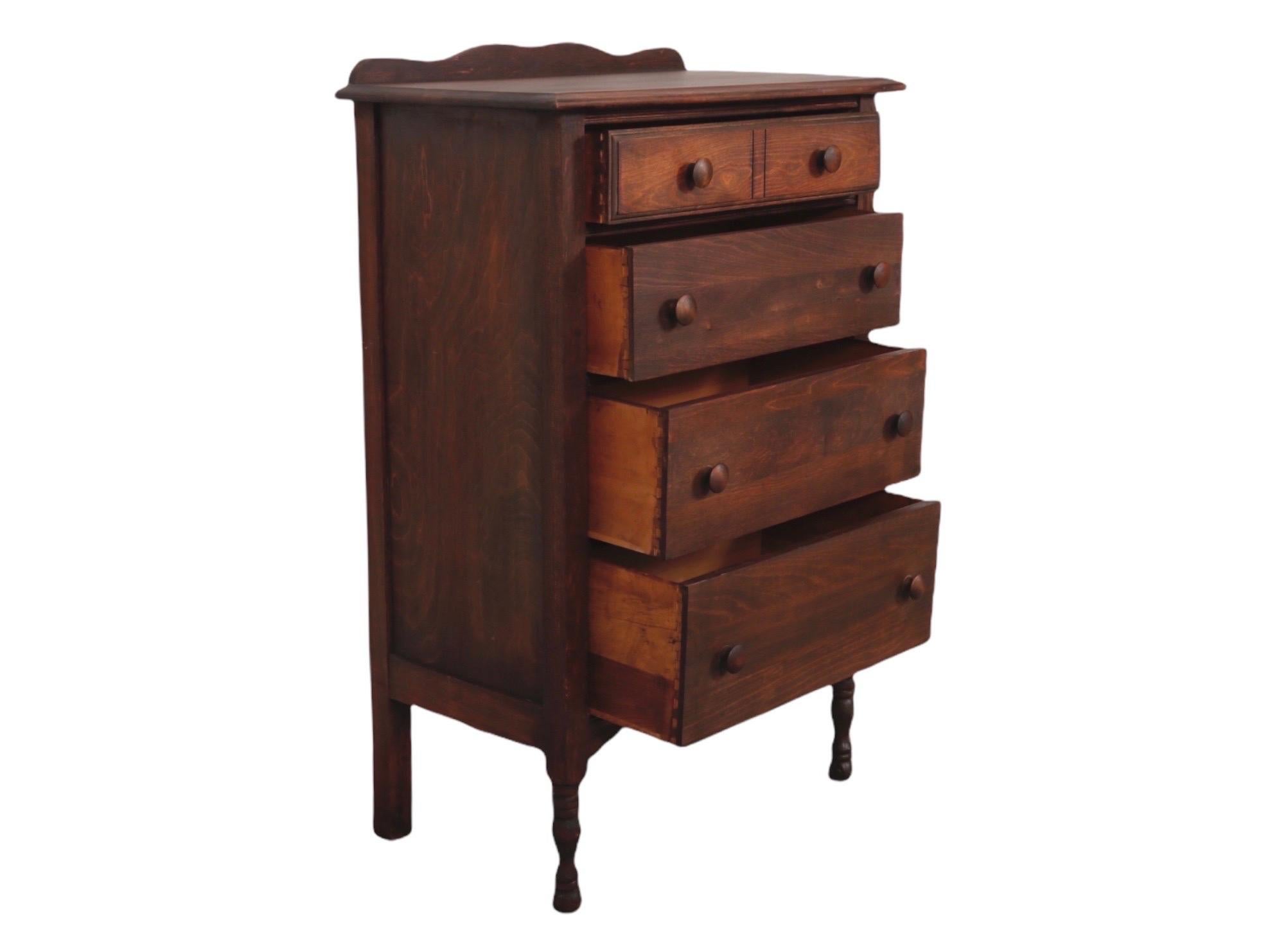 A petite standing chest of drawers, trimmed on top with a slender serpentine back splash. Four hand dovetailed drawers open with mushroom knob handles. The top drawer front is carved to give the look of two drawers. Front turned legs finish in bun