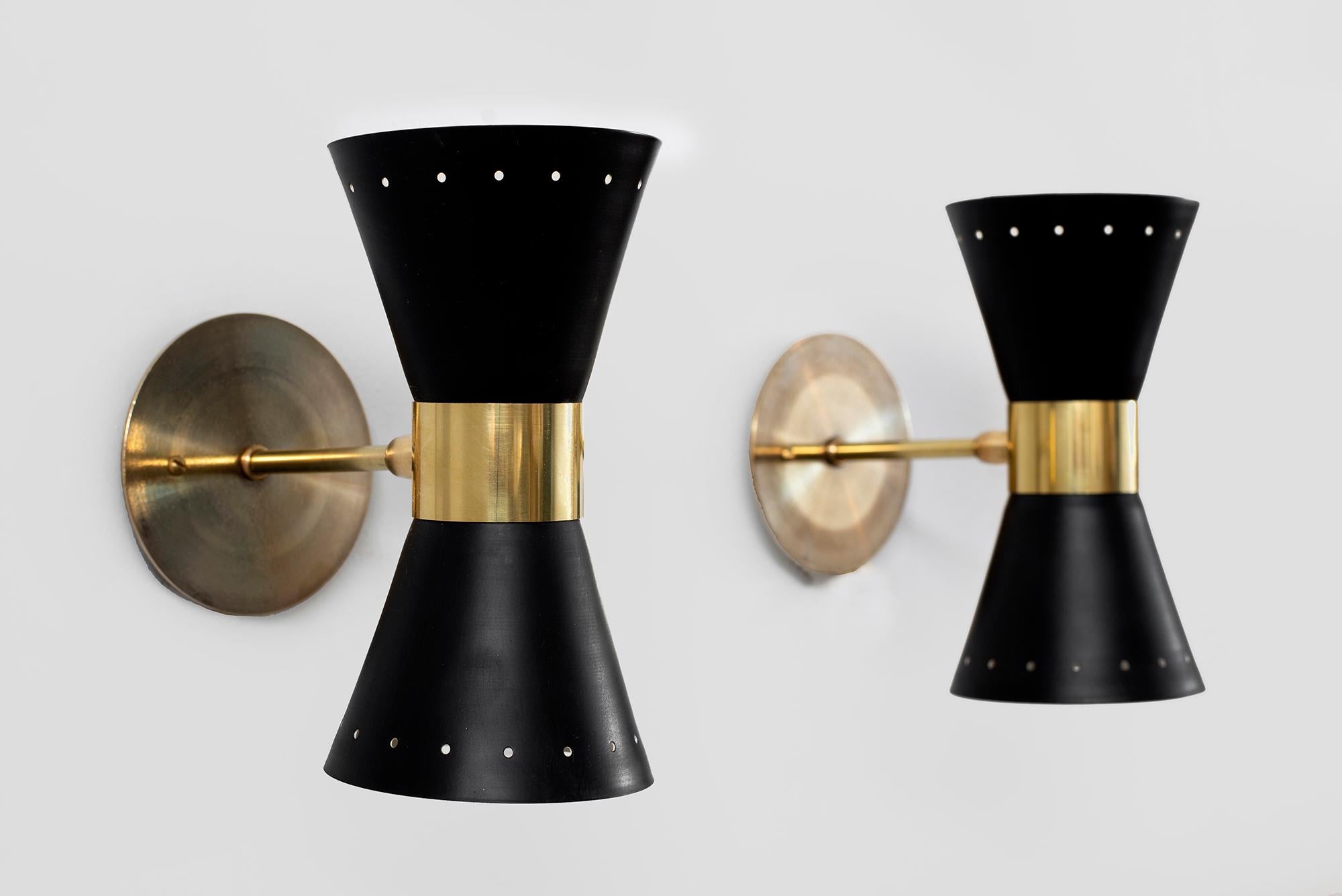 Petite in scale - metal sconces in the style of Stilnovo, newly produced in Italy. 
Black perforated metal shade with brass detailing and back-plate.
Sconces shine both up and down light.
Wired to American standards.
 
Measures: W 4 3/4”
D 8