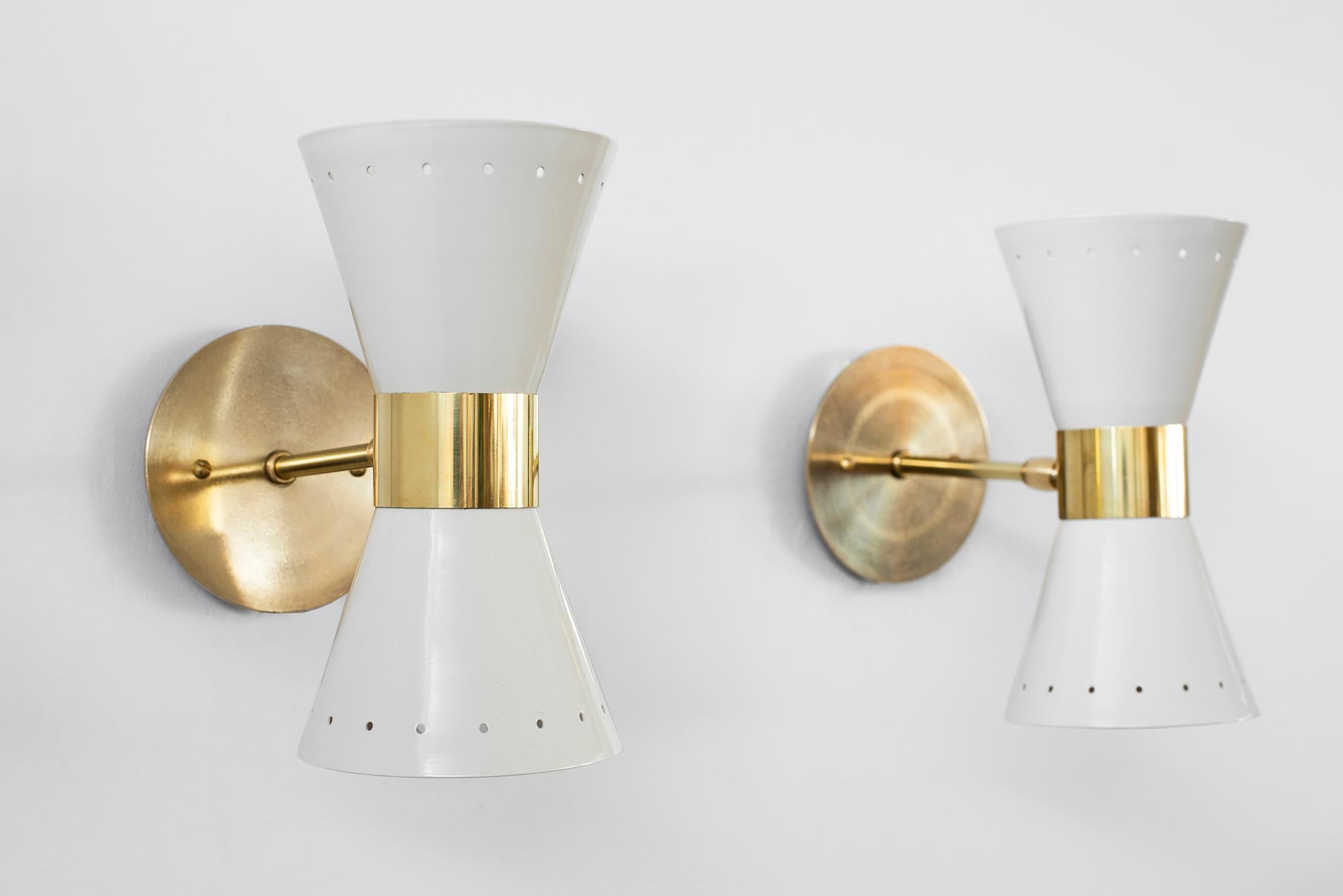 Petite in scale, metal sconces in the style of Stilnovo, newly produced in Italy. 
Creamy white perforated metal shade with brass detailing and back-plate.
Sconces shine both up and down light.
Wired to American standards.

Measures: W 4