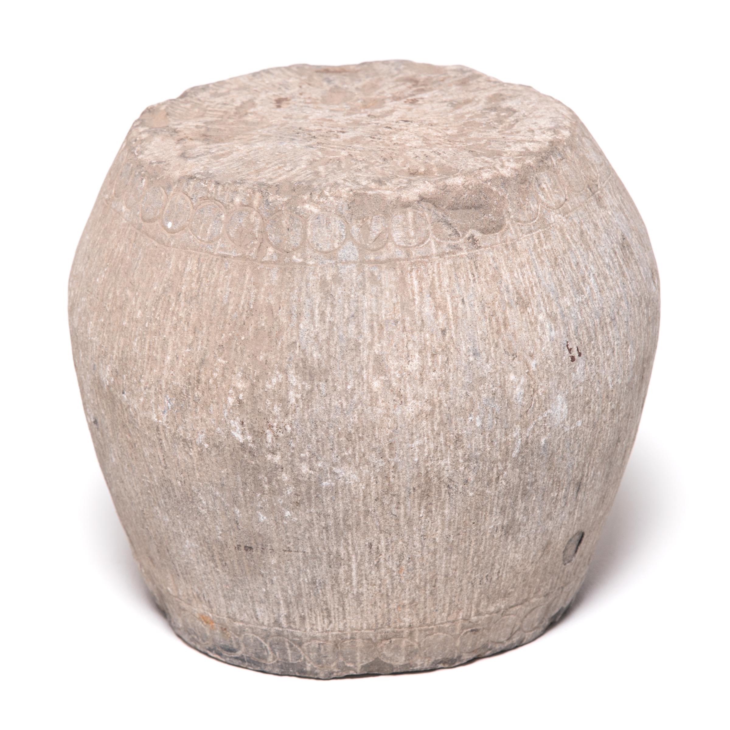 Look closely and you can just make out the hand-carved details that once made this small stone stool resemble a drum. A ring of circles along the top and bottom imitates bosshead nails used to stretch a skin on an actual drum, and thin vertical