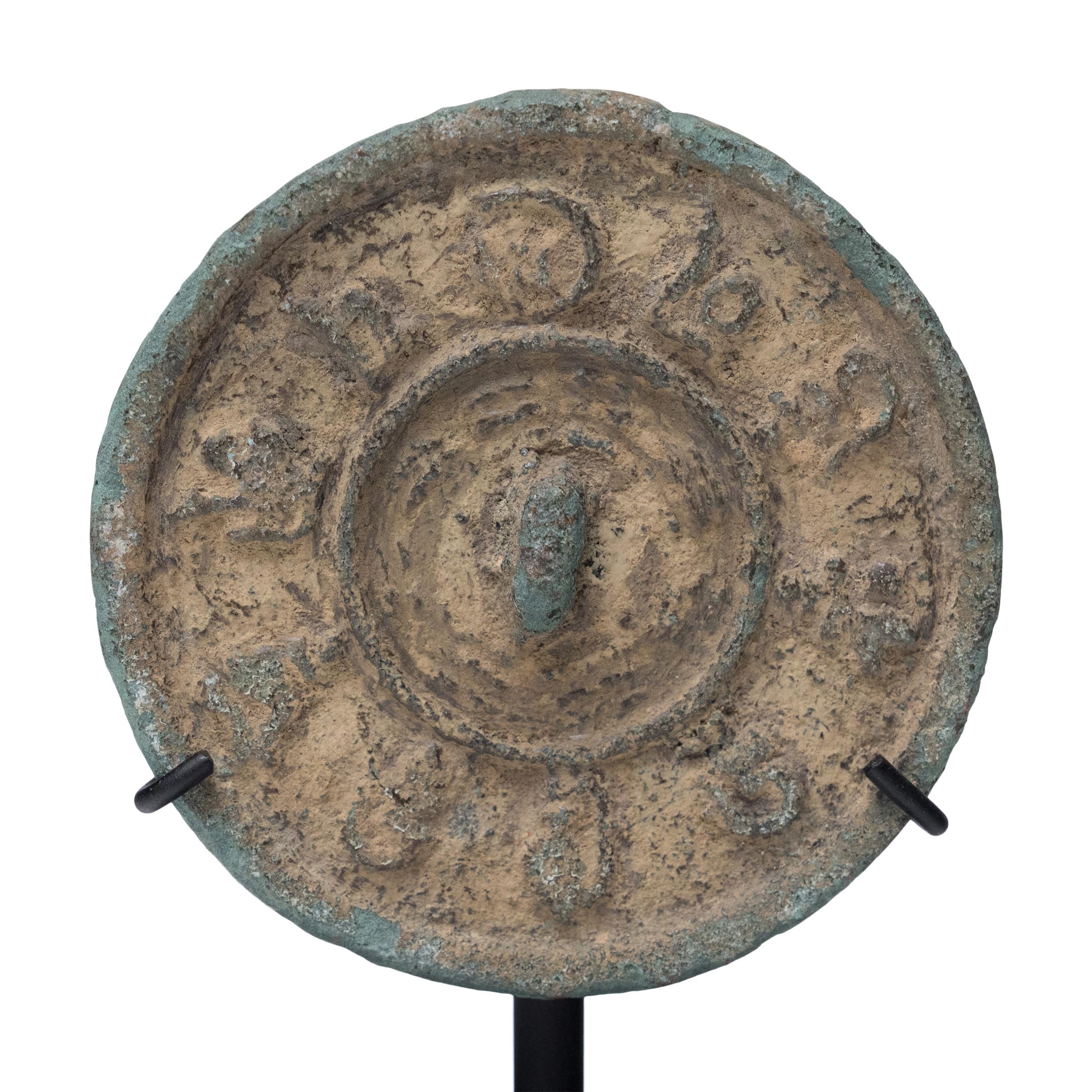 Cloaked in allover verdigris oxidization, this petite Chinese bronze mirror has the simple beauty and undeniable texture of an ancient object. Though an exact date is unknown, the mirror's raised inner ring and prominent relief decoration suggest it