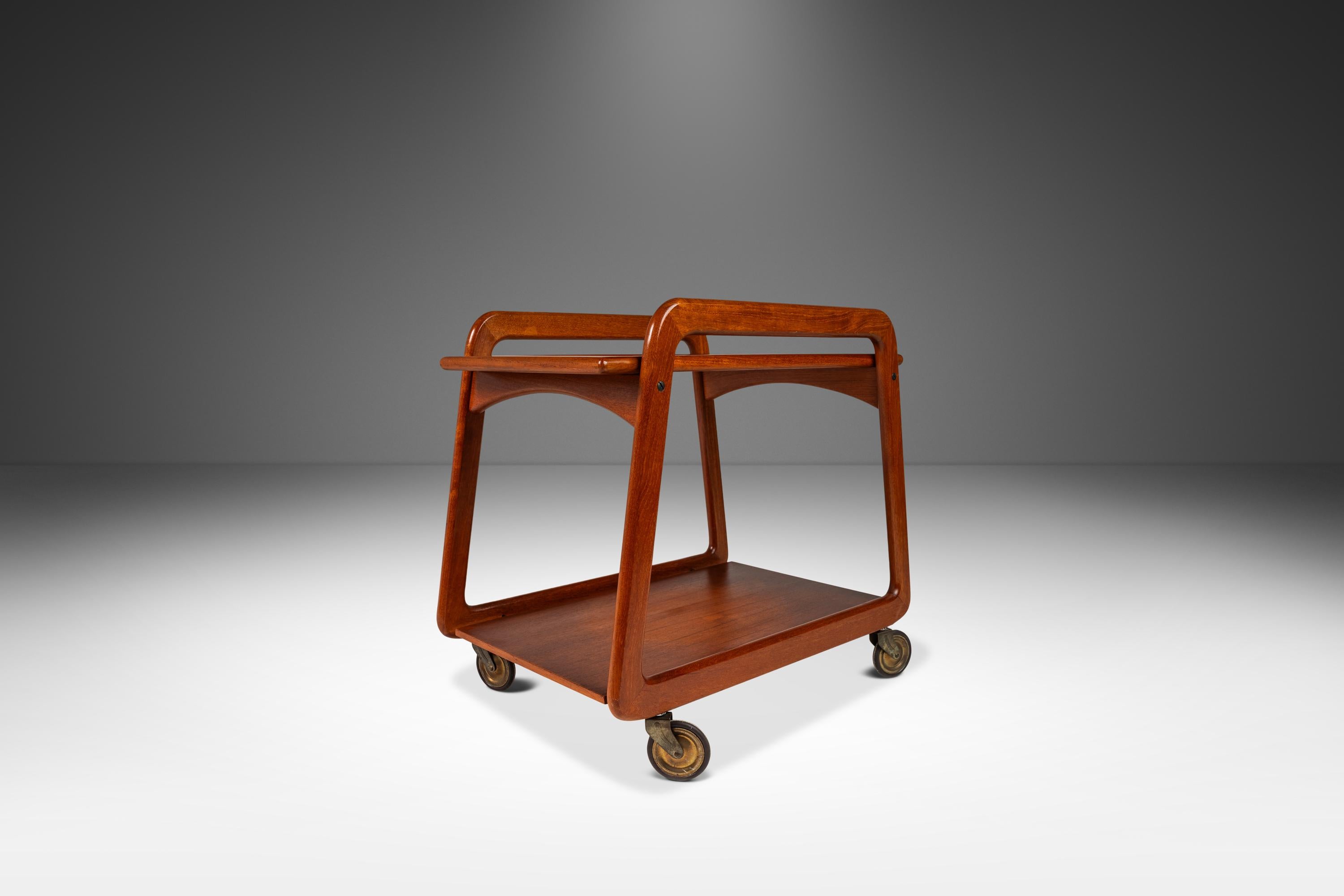 In egual misura funzionale e bello, questo eccezionale carrello da bar di produzione danese  è un must per i collezionisti alla ricerca del pezzo d'accento perfetto. Realizzato in teak massiccio, questo pezzo dal design intelligente presenta un