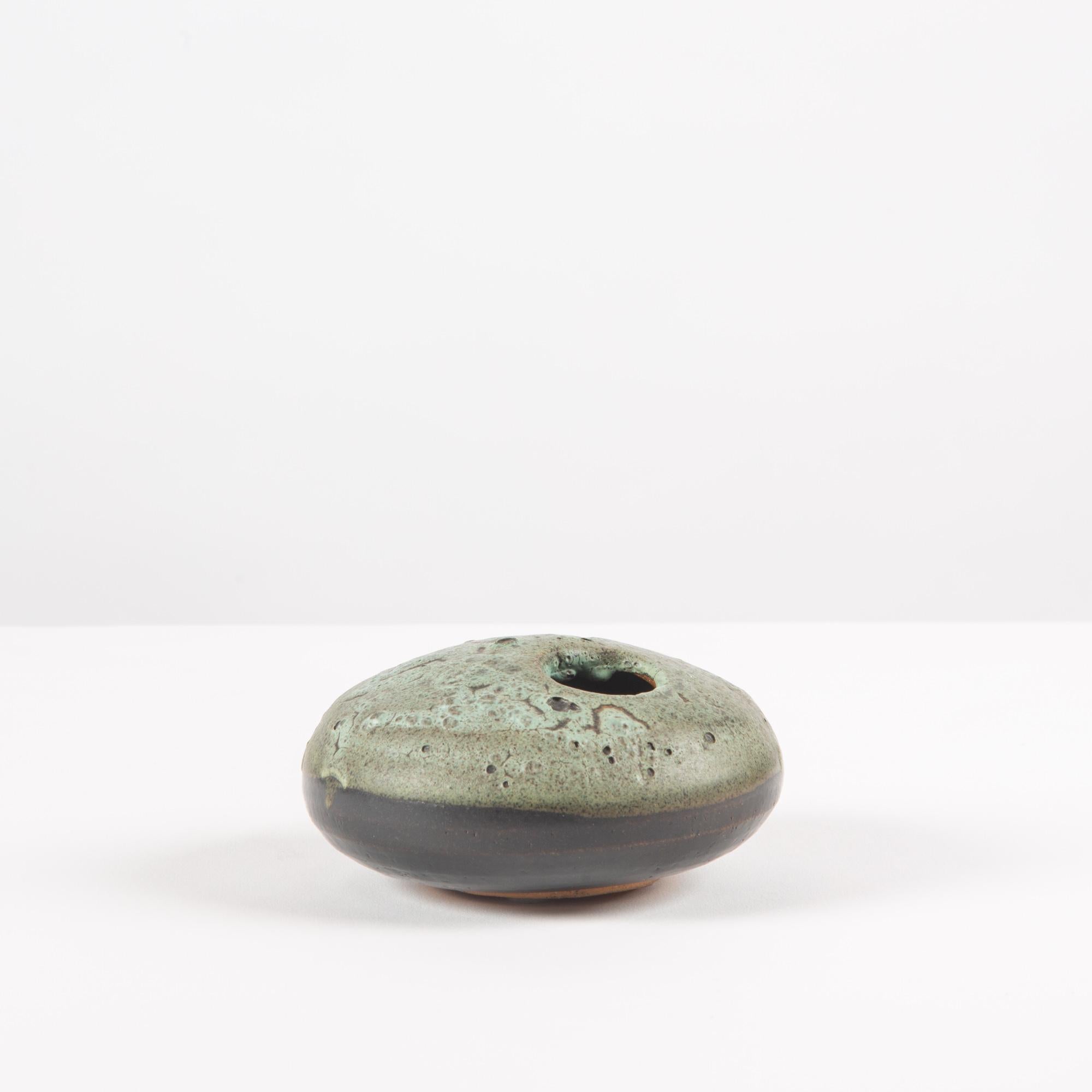 Petite round vessel features a two-tone glaze in seafoam and dark forest green. The top of the vessel is textured with a round opening off center to hold a few buds. Artist signature on the underside.

Dimensions: 4.75?