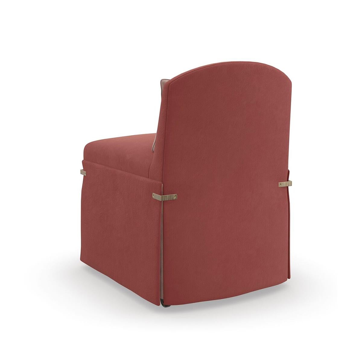 This petite seat calls to mind the exquisite detail and drape of a bustle dress, fashionable during the late 1880s. Its elegant silhouette features a low camelback and dressmaker skirt in a dusty rose fabric, cinched together by textured metal