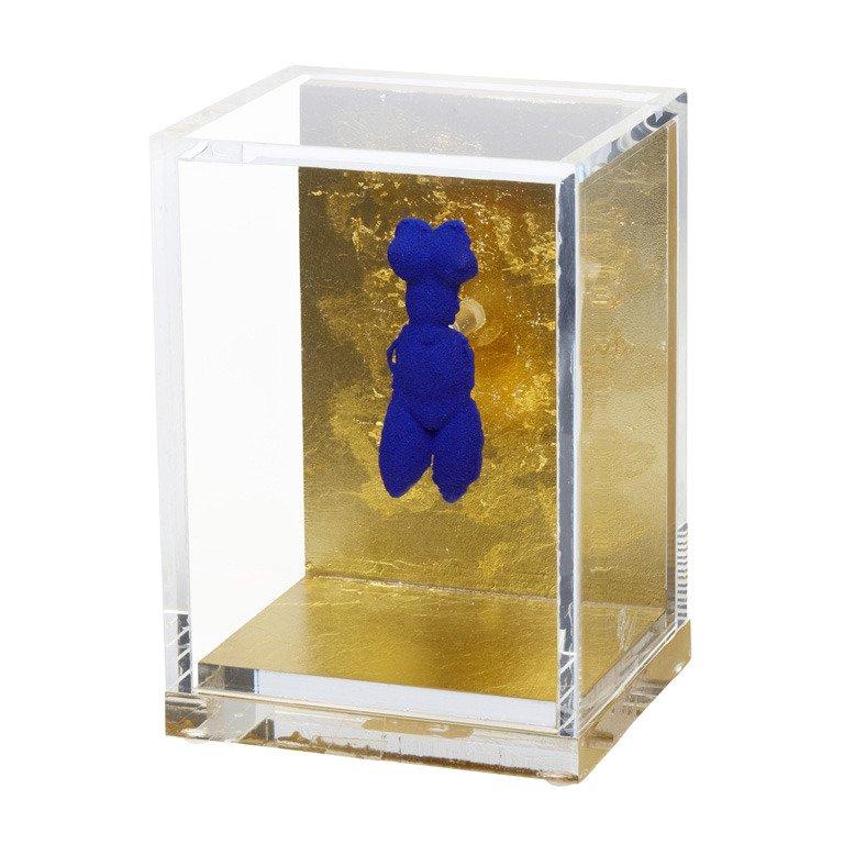 Petite Vénus Bleue (1956/57) by Yves Klein features a brass pin covered in International Klein Bleue (IKB) pigment and shaped as one of Klein's Vénus Bleue figures. The pin is mounted perpendicularly to a gold-leafed, acrylic backdrop that attaches