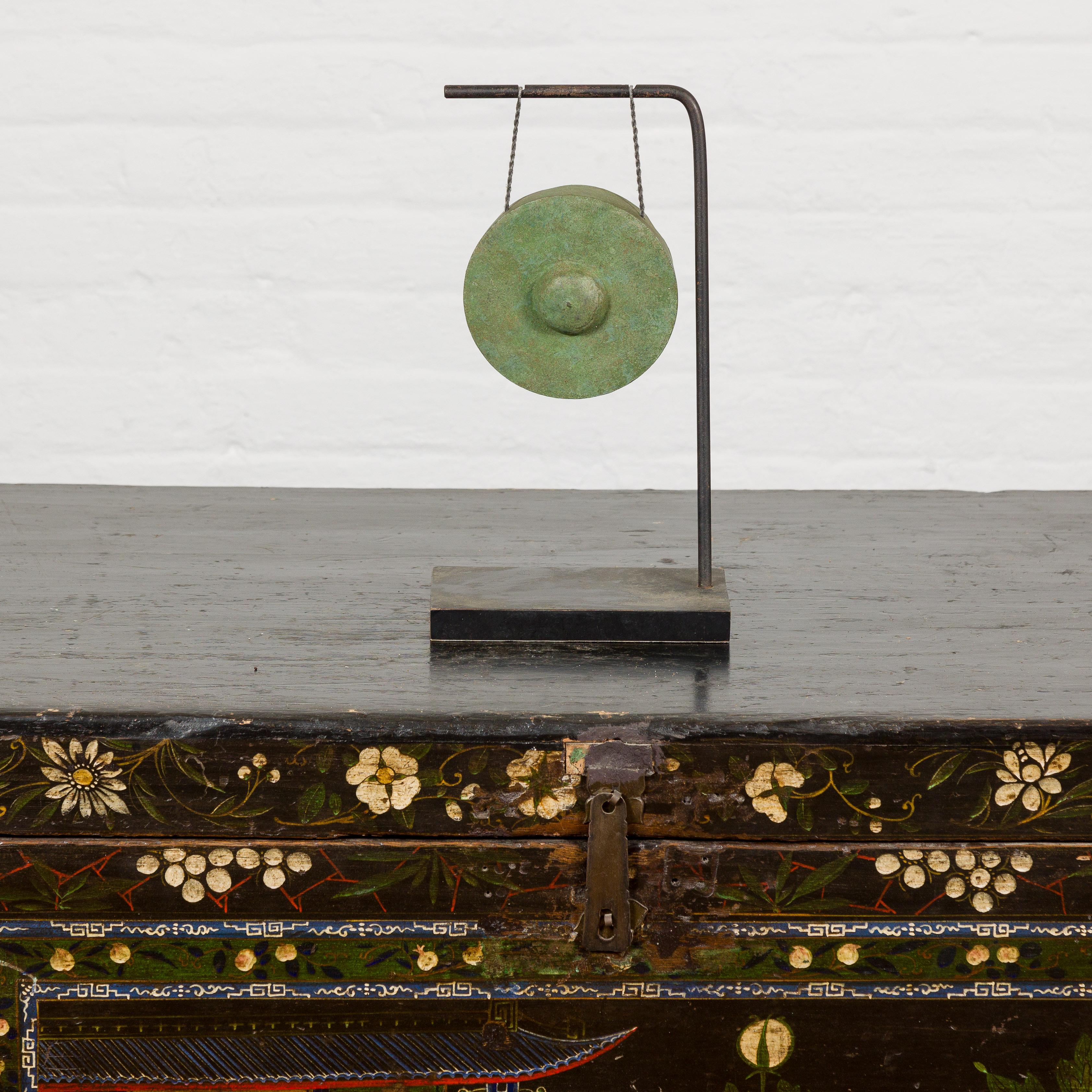 Ein zierlicher Bronzegong mit Grünspanpatina, montiert auf einem schwarzen Metallsockel. Dieser zierliche Bronzegong ist ein Zeugnis der Schönheit von Einfachheit und Handwerkskunst. Der Gong aus Bronze, der im komplizierten Wachsausschmelzverfahren
