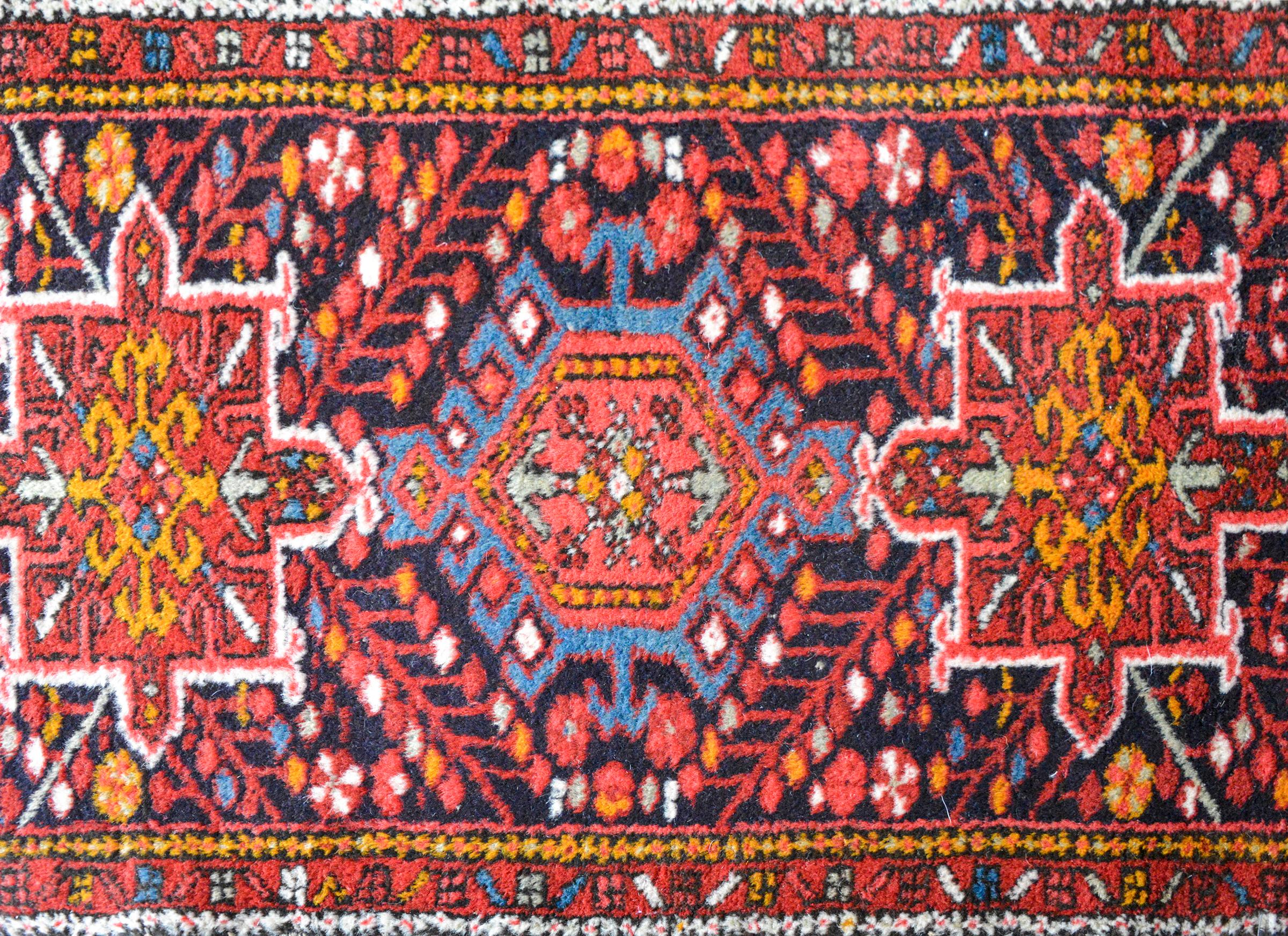 A vintage petite Persian Karadja rug with three stylized floral medallions woven in red, orange, white, and light indigo, against a crimson black background and surrounded by multiple thin floral partnered stripes.


