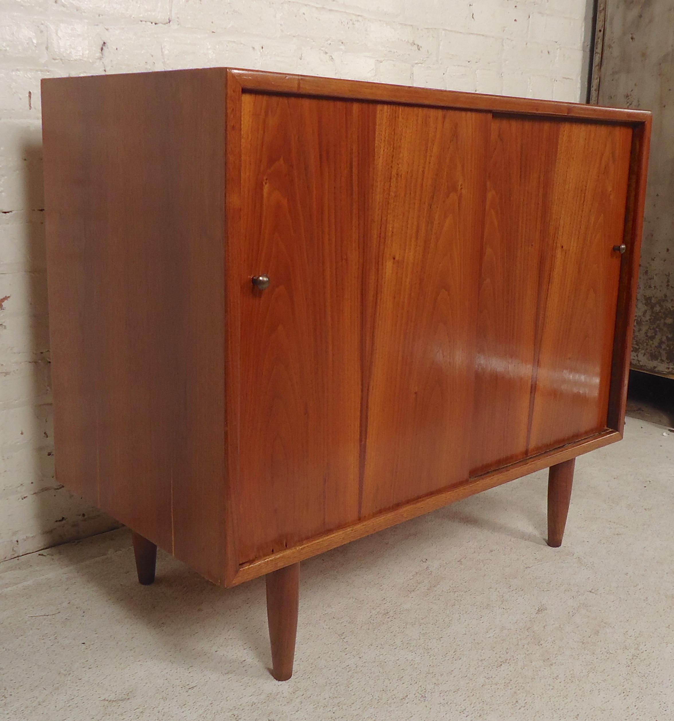 Mid-Century Modern two-door cabinet in warm walnut grain. Small brass handles and tapered legs.

(Please confirm item location - NY or NJ - with dealer).
  