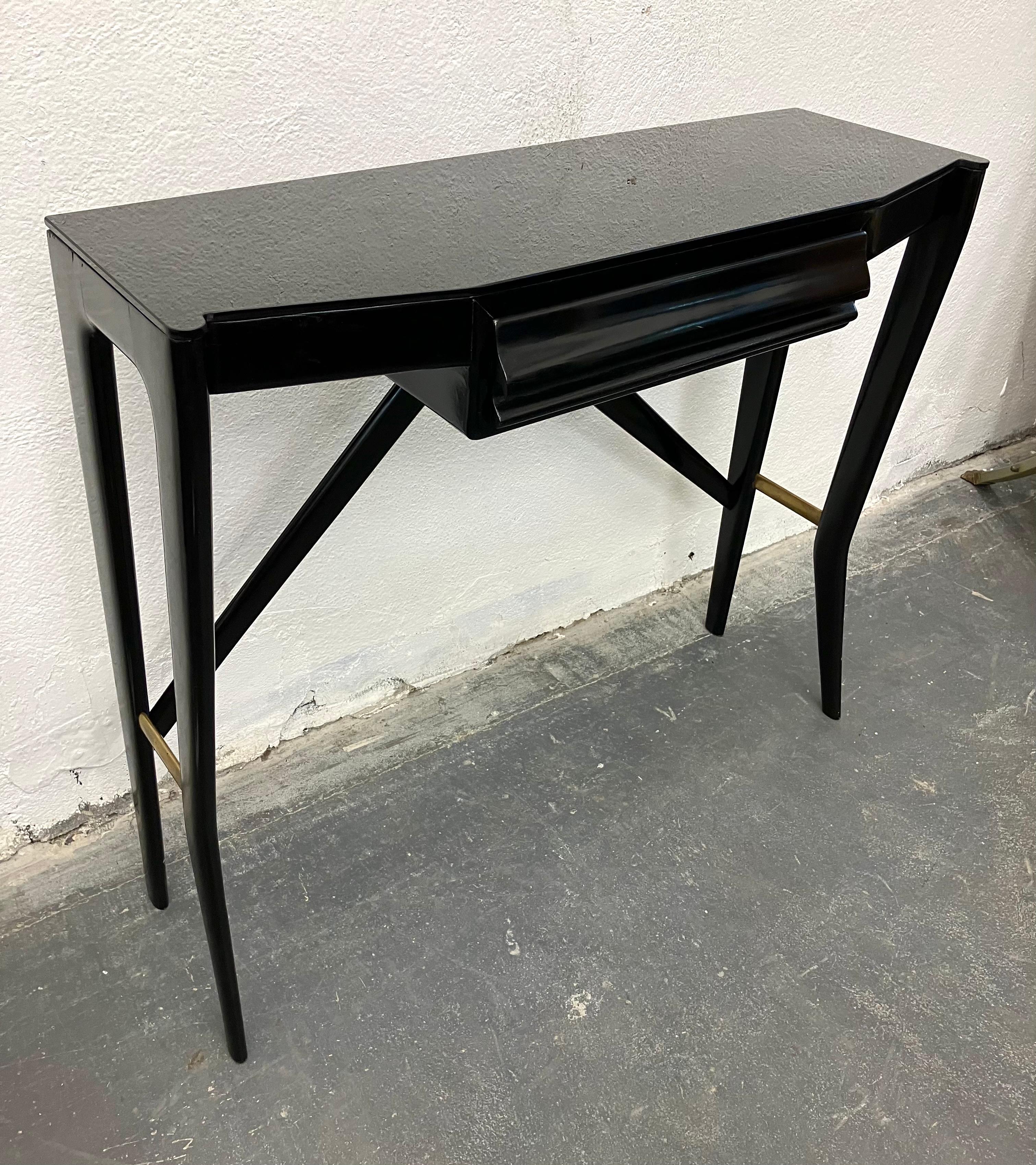 Chic small console in black piano lacquer, with single inset drawer, raised on sculpted legs and stretchers. The side brass supports add an elegant material contrast. 

Unmarked and designer unknown, this table was retailed by La Permanente Cantu,