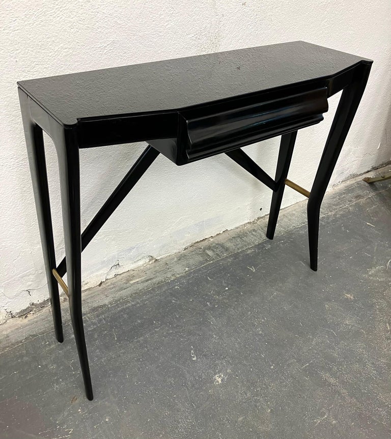 Chic small console in black piano lacquer, with single inset drawer, raised on sculpted legs and stretchers. The side brass supports add an elegant material contrast. 

Unmarked and designer unknown, this table was retailed by La Permanente Cantu,