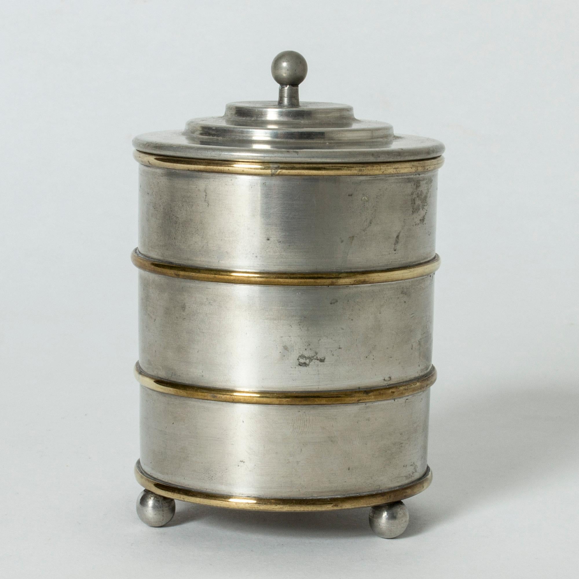 Beautiful pewter jar from Herman Bergman, with ball fett and a small round knob on the lid. Decorative, contrasting, horizontal brass stripes.