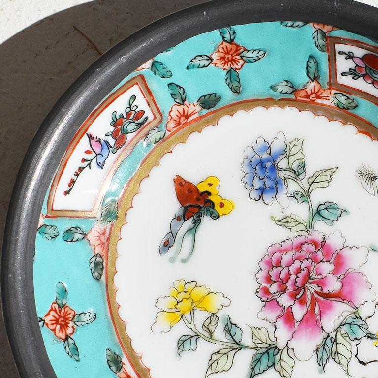 An unusual pewter-encased ceramic bowl. Decorated with brightly colored hand-painted flowers and butterflies, this small decorative dish will be an excellent accent piece on a coffee or side table. The bowl itself has a bright almost turquoise-blue