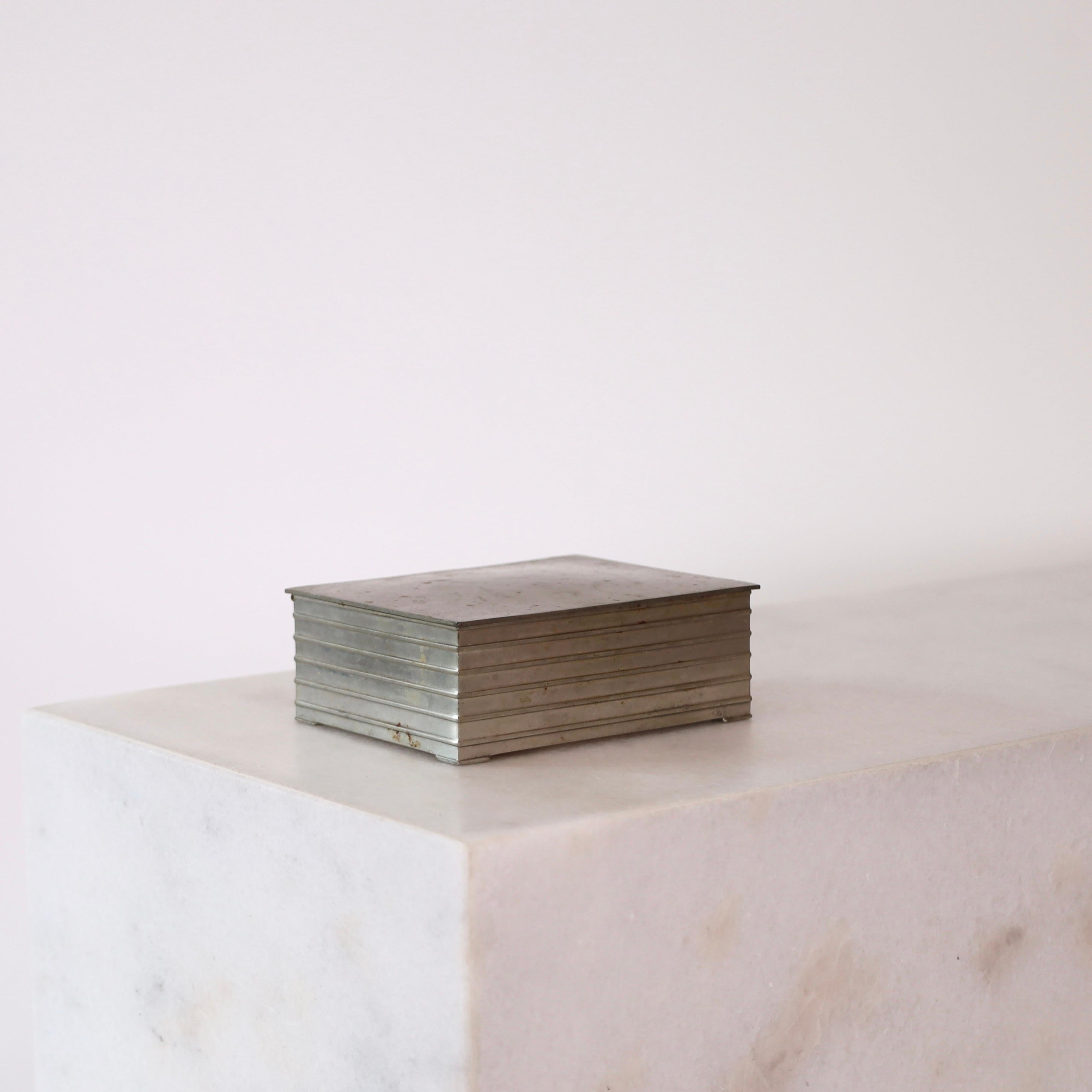 A pewter box designed by Ellen Schlanbusch for Just Andersen in the 1950s. An elegant piece for a beautiful place.

* A lidded box in pewter with a wooden inner box. Originally cigarette box.
* Designer: Ellen Schlanbusch
* Style: 2533
*