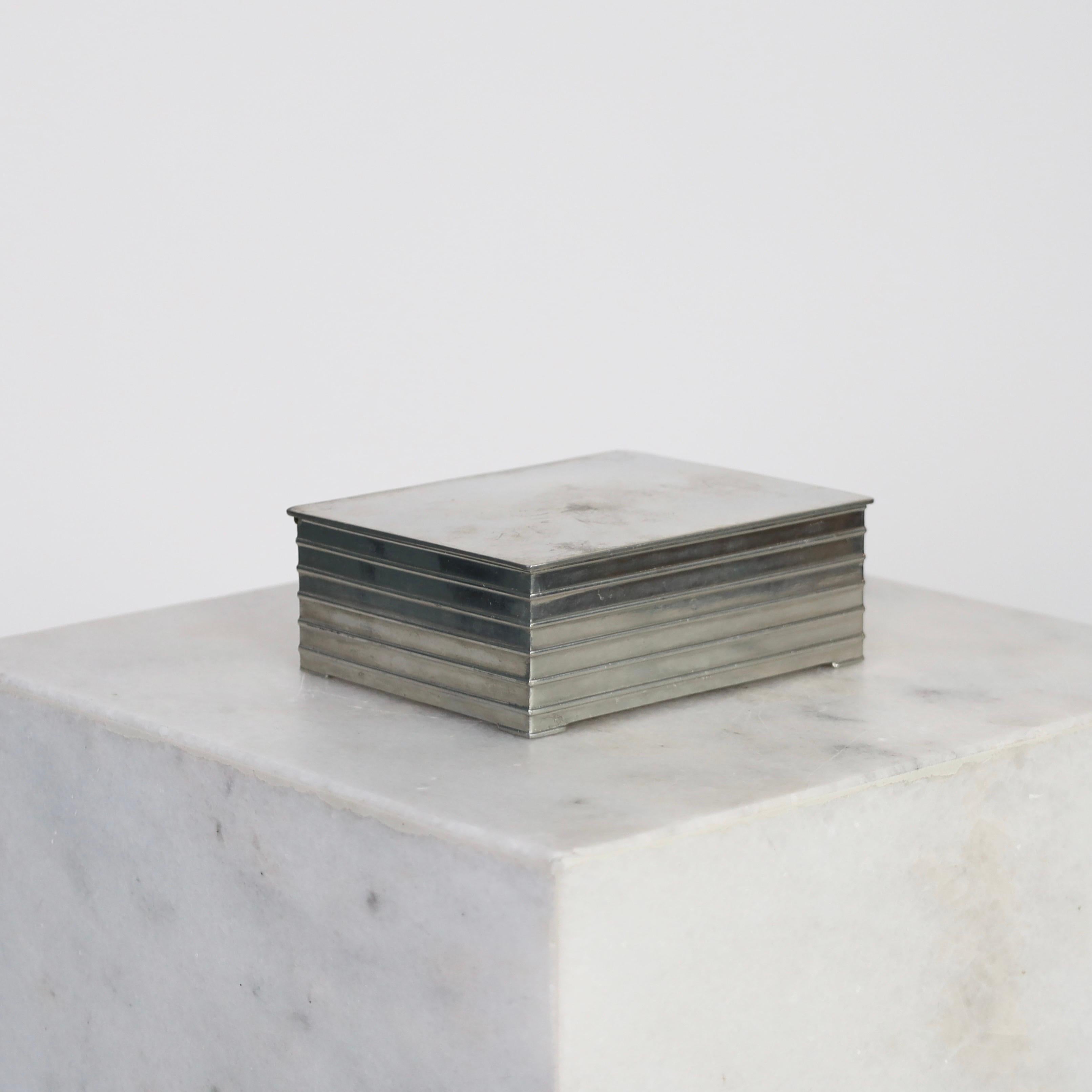 A pewter box designed by Ellen Schlanbusch for Just Andersen in the 1950s. An elegant piece for a beautiful place.

* A lidded box in pewter with a wooden inner box. Originally cigarette box.
* Designer: Ellen Schlanbusch
* Style: 2533
*