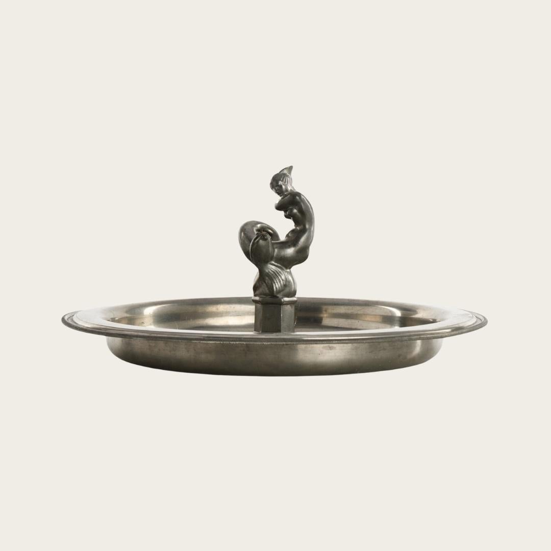 Inspired by Just Andersen’s 1930s Danish design, this pewter dish features a Swedish Grace relief showcasing a nude mermaid and fish at its center. The piece is unmarked.