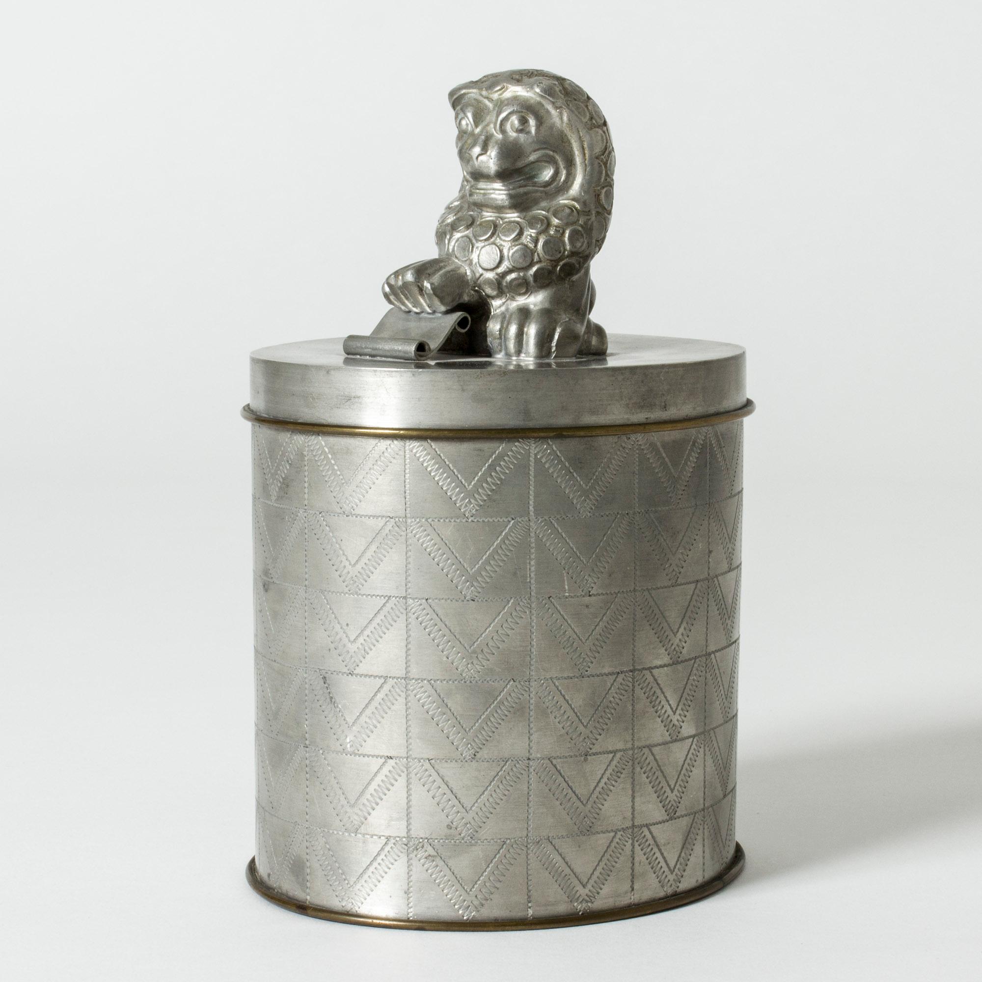 Amazing pewter jar by Anna Petrus, with a line of brass encircling the base and lid. Expressive lion on the lid, body decorated with a graphic pattern.