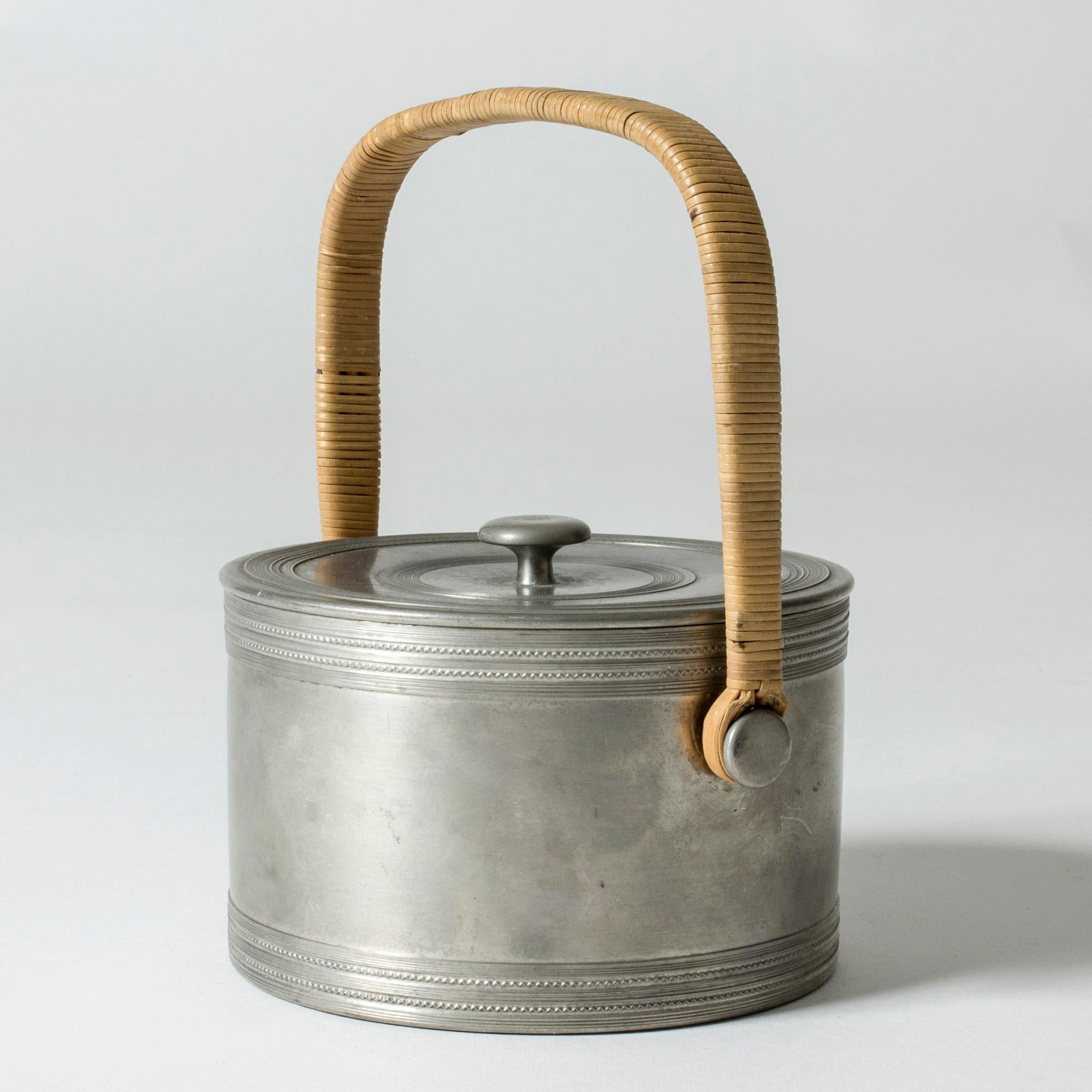 Elegant pewter jar by Estrid Ericson, with beautiful matte patina. Rim and lid decorated with a subtle pattern. Handle wound with blonde rattan for a nice contrast.