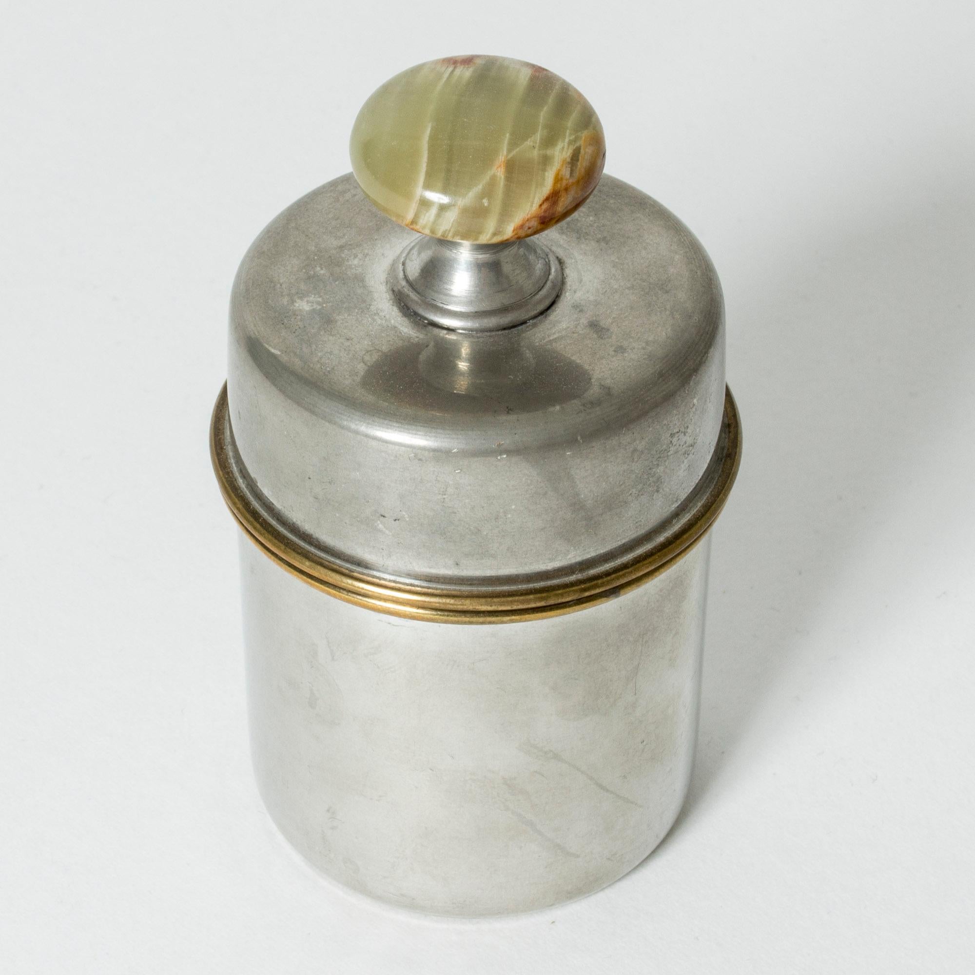 Lovely pewter jar by Estrid Ericson, in a cylinder form. Brass rims around the edges, adorned with an elevated, green agate stone in a knob form.
