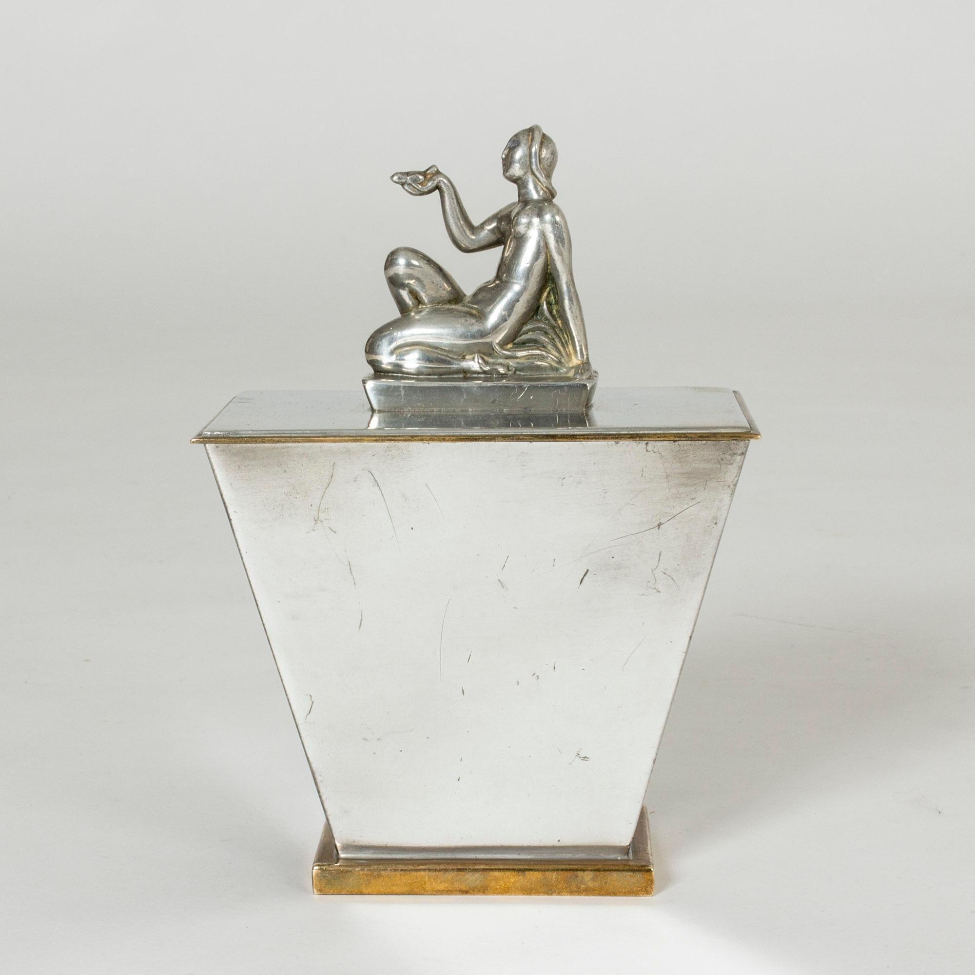 Striking pewter jar by Oscar Antonsson, with brass at the base and around the edge of the lid. Adorned with a beautifully sculpted kneeling woman.