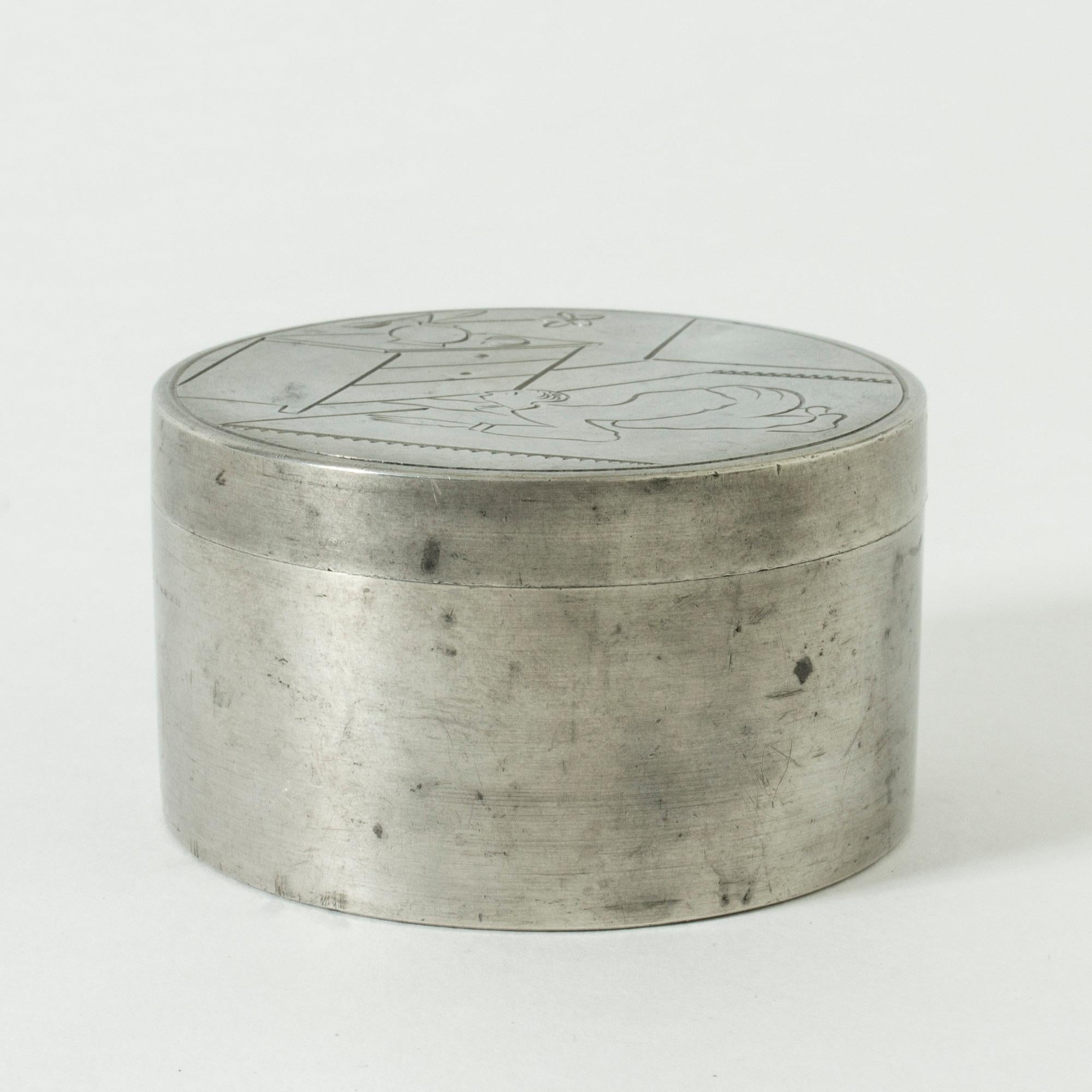 Small round pewter jar by Sylvia Stave, with clean lines. The humoristic motif on the lid, showing a man on the floor, peering in under a chest of drawers, tells us it is intended for the safe keeping of cufflinks. 
  