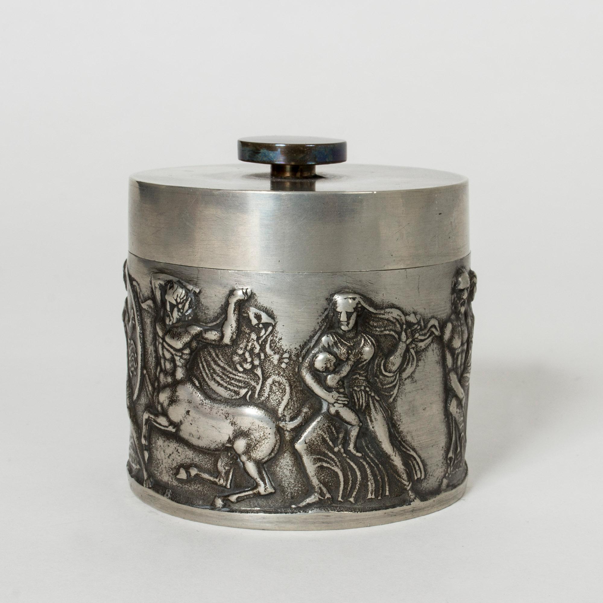 Pewter jar with brass knob. Designed by Herman Bergman, who was the founder of Herman Bergman’s Fine Art Foundry, purveyor to the Royal Court. A dramatic scene with centaurs, a warrior and a woman with a baby is depicted on the body of the jar.