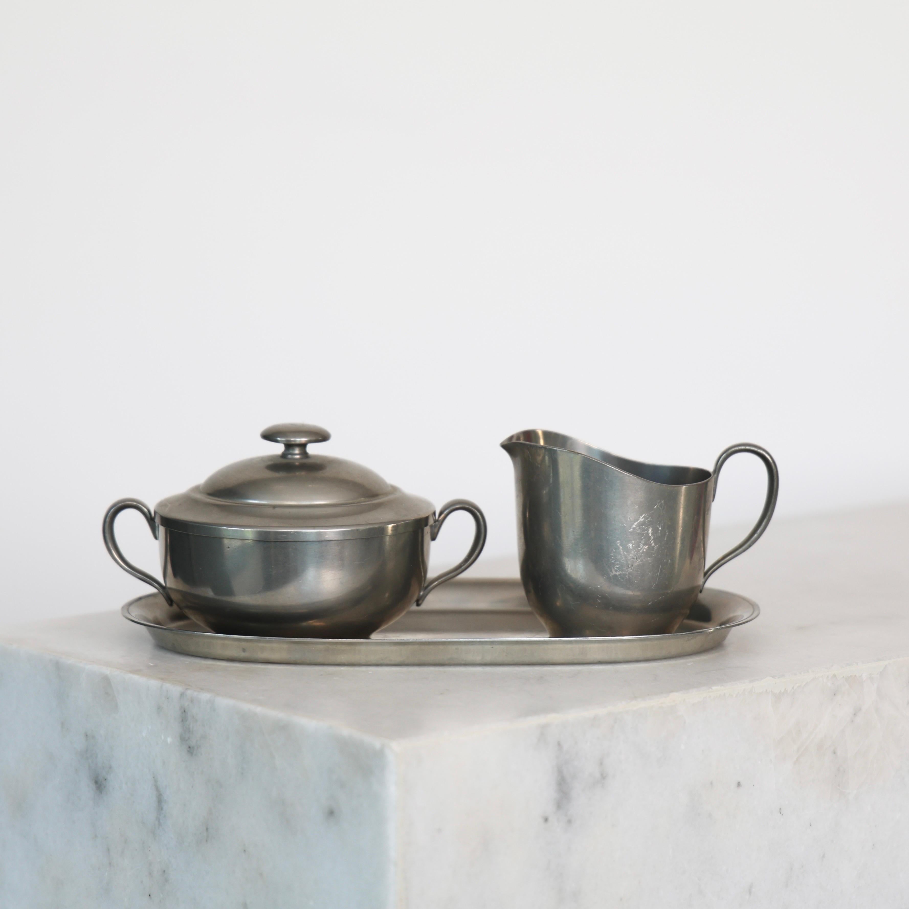 Pewter Sugar Jar & Creamer made by Just Andersen in the 1920s. An exquisite set for a beautiful table.

* Set (3) of pewter lidded sugar jar and creamer on tray 
* Designer: Just Andersen
* Style: 1559, 1560 & 1560B
* Year: 1918-1929
* Condition: