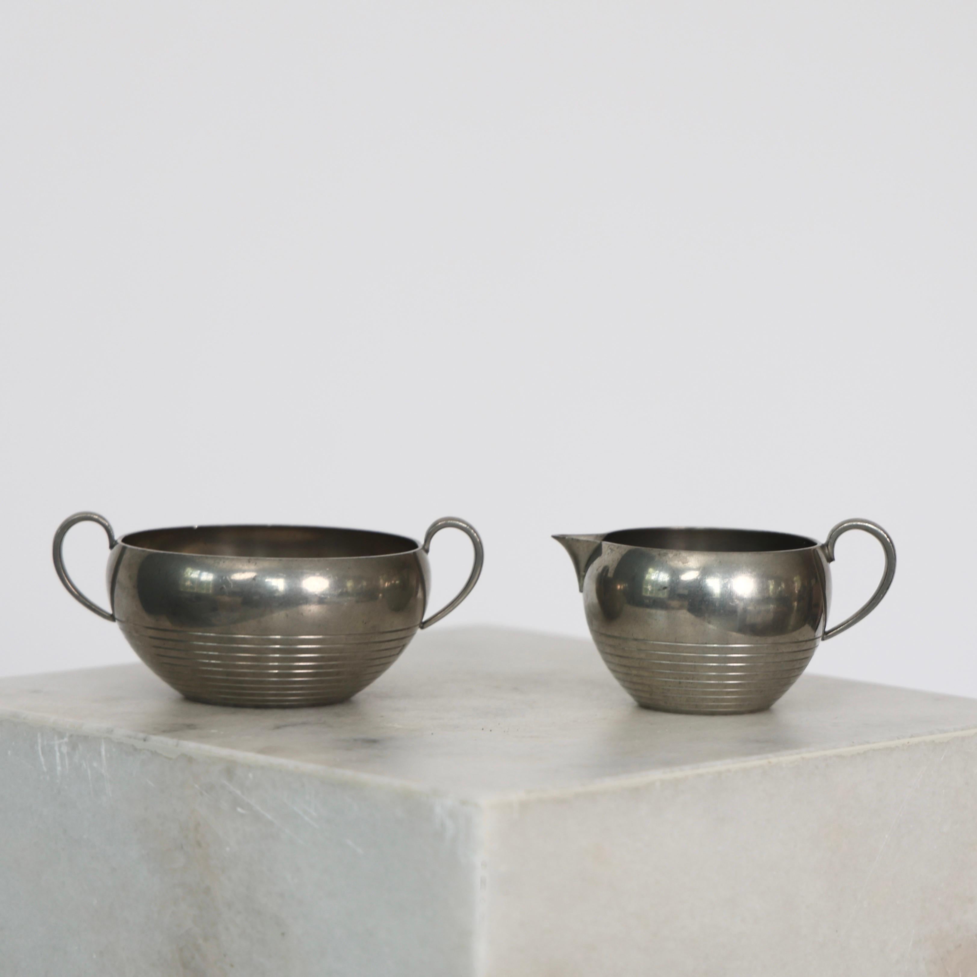 Elegant set of Pewter Sugar Jar & Creamer made by Just Andersen in the 1930s. 

* Set (2) of pewter sugar jar and creamer with lugs and round chasings at the bottom
* Designer: Just Andersen
* Style: 2158
* Year: 1939
* Condition: Good vintage