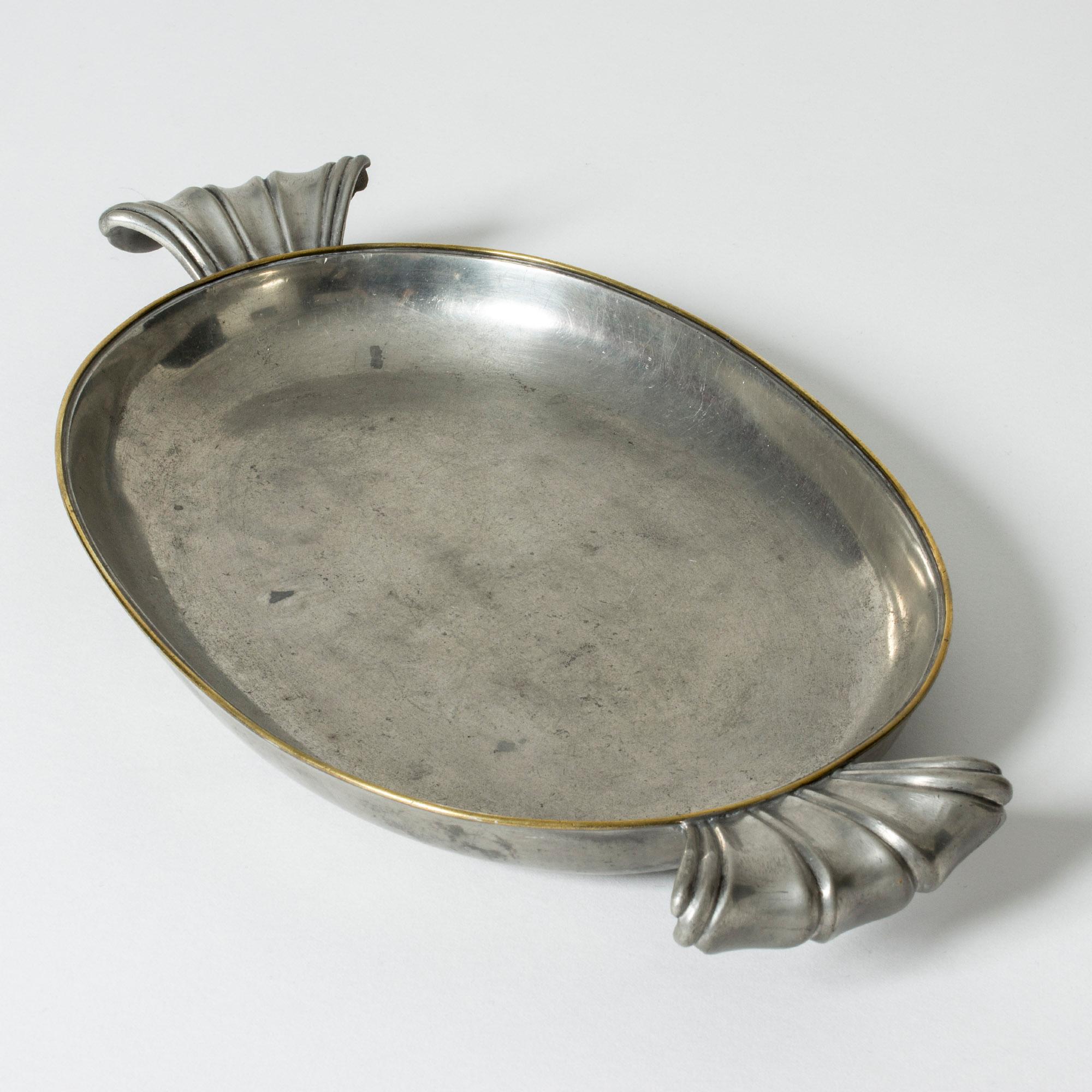 Beautiful pewter tray from Svenskt Tenn. Oval form with a brass rim around the edge. Large, decorative handles.