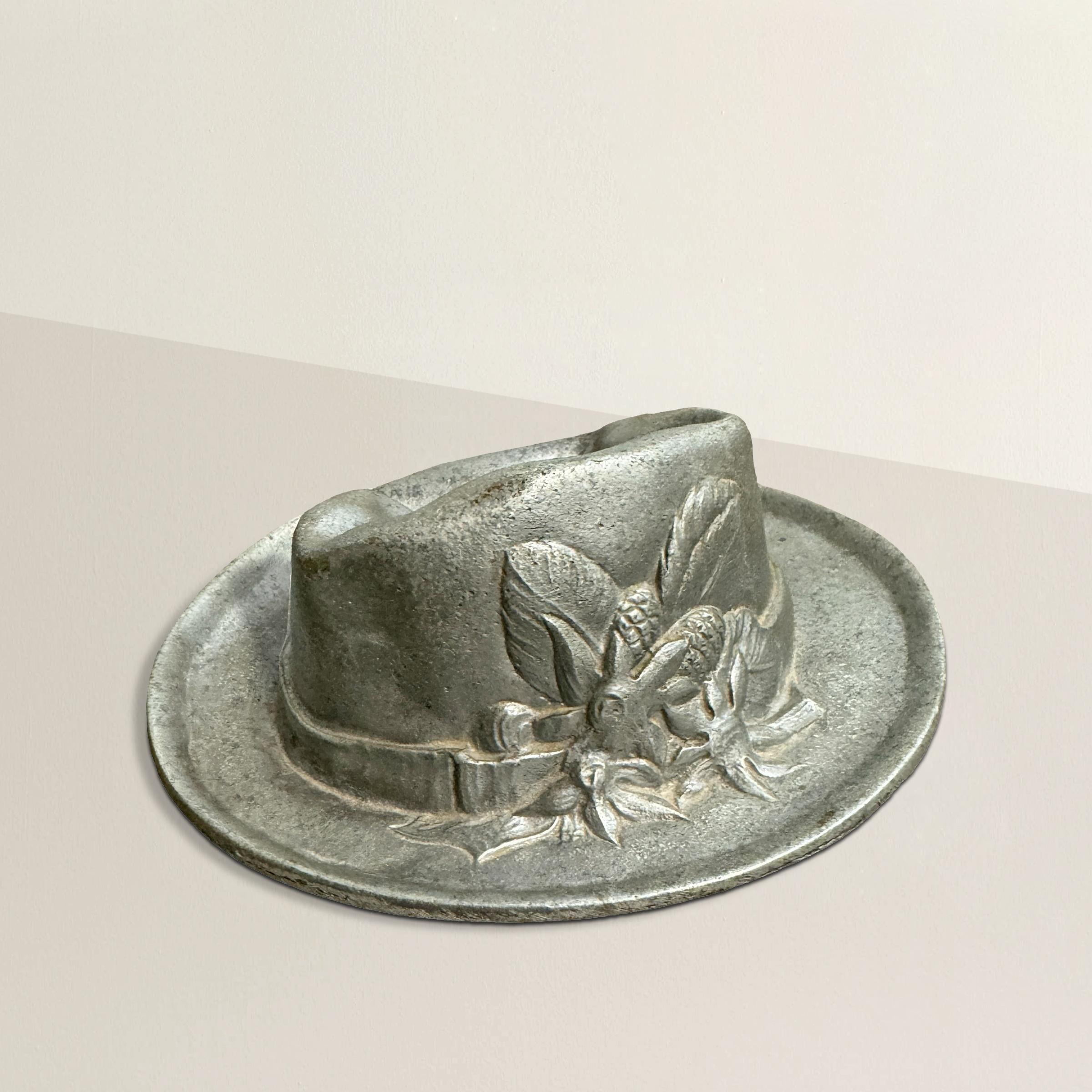 Questo piatto in peltro della metà del XX secolo è un pezzo affascinante e funzionale a forma di cappello tirolese, con tanto di corona a fossette. Perfetto per contenere chiavi, spiccioli o qualsiasi altro piccolo oggetto, è un contenitore ideale