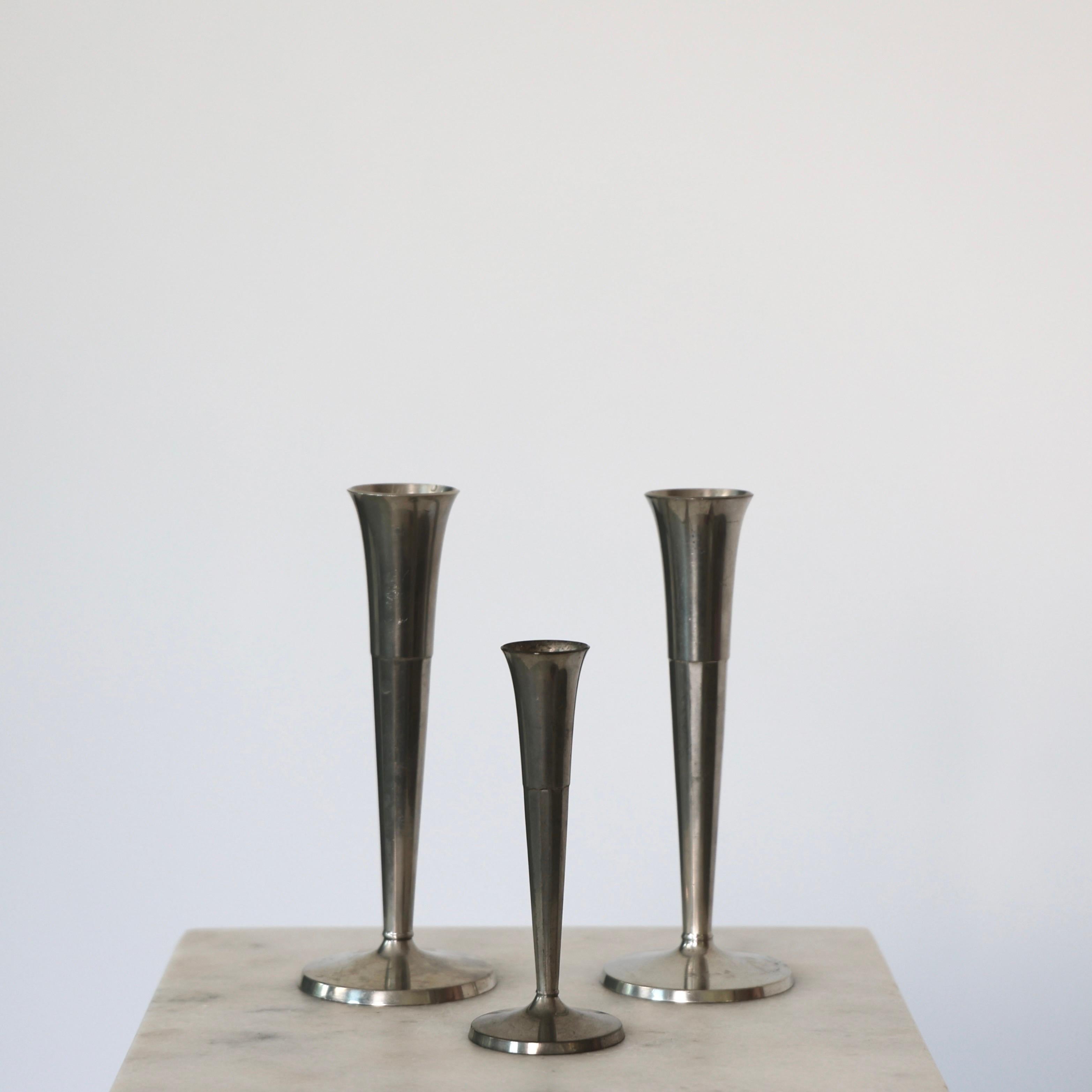 Elegant Pewter Vase Trio designed by Ellen Schlanbush for Just Andersen in the early 1950s.

* Set (3) of tall cannellated pewter vases on round foot
* Designer: Ellen Schlanbusch
* Style: 2645 & 2646
* Year: 1952
* Condition: Good vintage