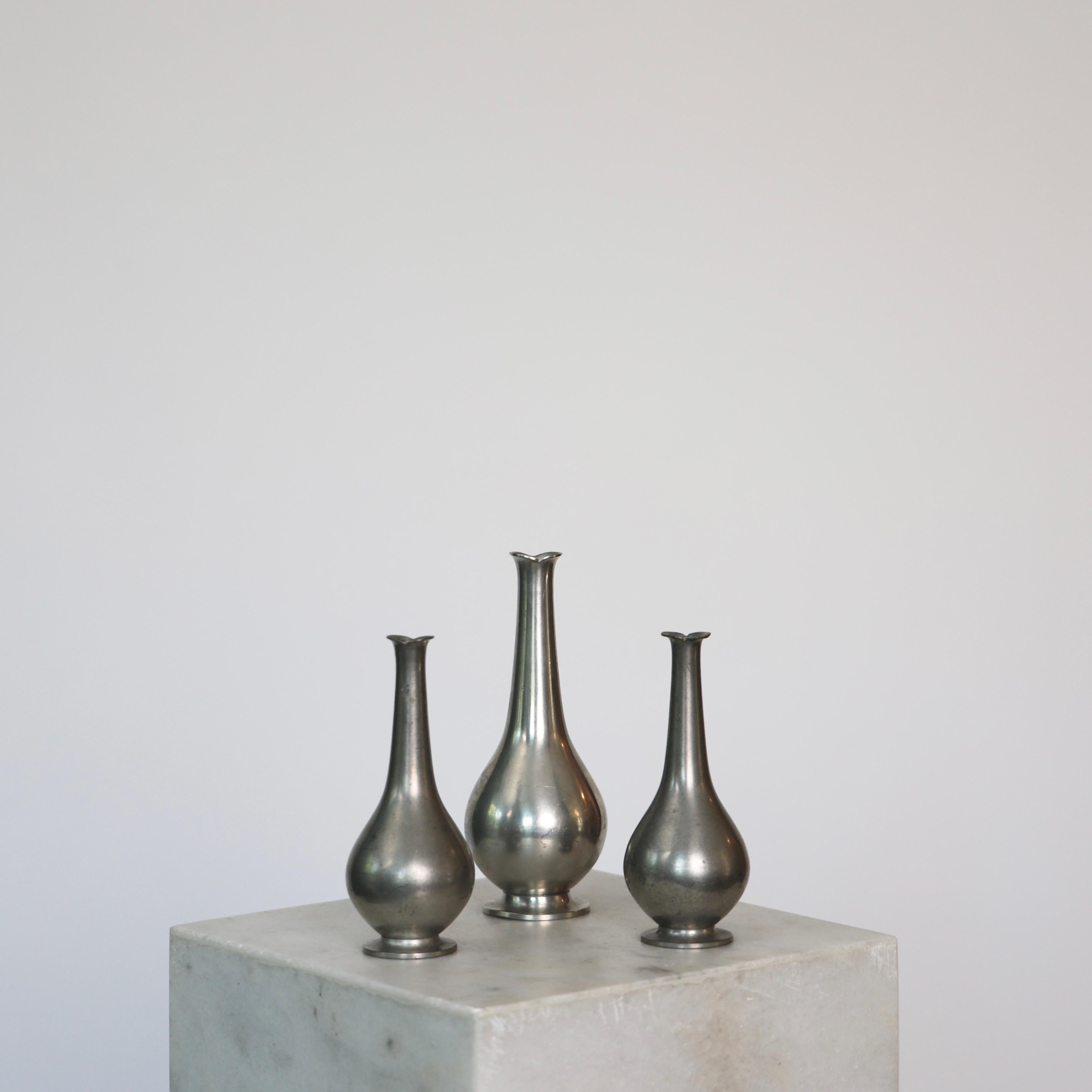 Trio of Pewter Vases made by Just Andersen in the 1920s. 

* Set (3) of round pewter vases with slim necks - two small, one larger
* Designer: Just Andersen
* Manufacturer: Just Andersen
* Style: 1457 (two sizes).
* Year: 1918-1926
* Condition: Good