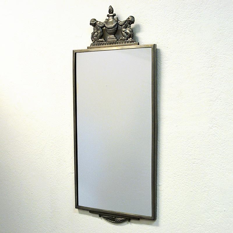 A stunning classic vintage Swedish Modern mirror by Oscar Antonsson in pewter from Ystad Metall 1929. Decorative top frame showing two children kneeling on one leg next to a large vase. This is a very rare mirror with great details in very good