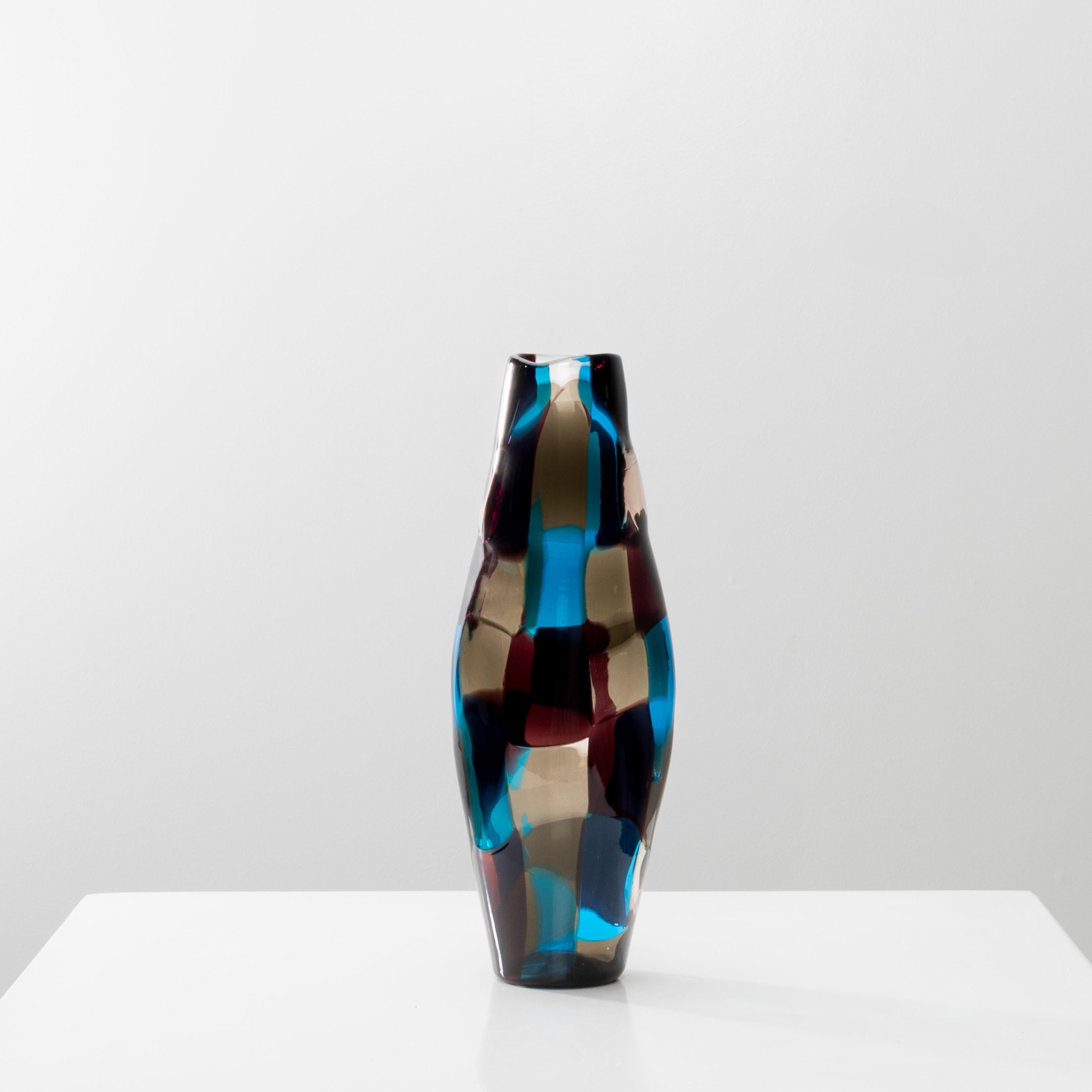 “Carrot” shaped pezzato vase, irregular section. The base and the neck are round.
Made up of an arrangement of ash gray, sky blue, wine red and clear tesserae.
This chromatic combination is sometimes called “Venezia”
Signature – round “venini murano