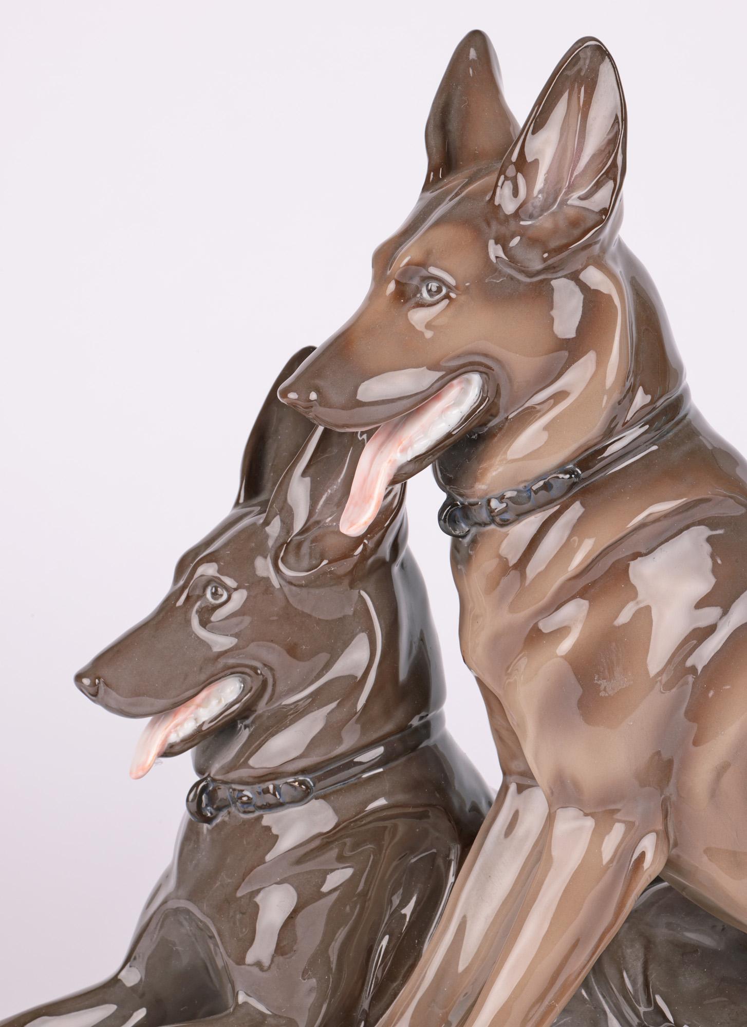 A fine German porcelain group of two German Shepherd dogs by Pfeffer Gotha and dating from the early to mid 20th Century. The dogs are presented raised on a an oval shaped base with one dog lying while the other sits alongside both with their eyes