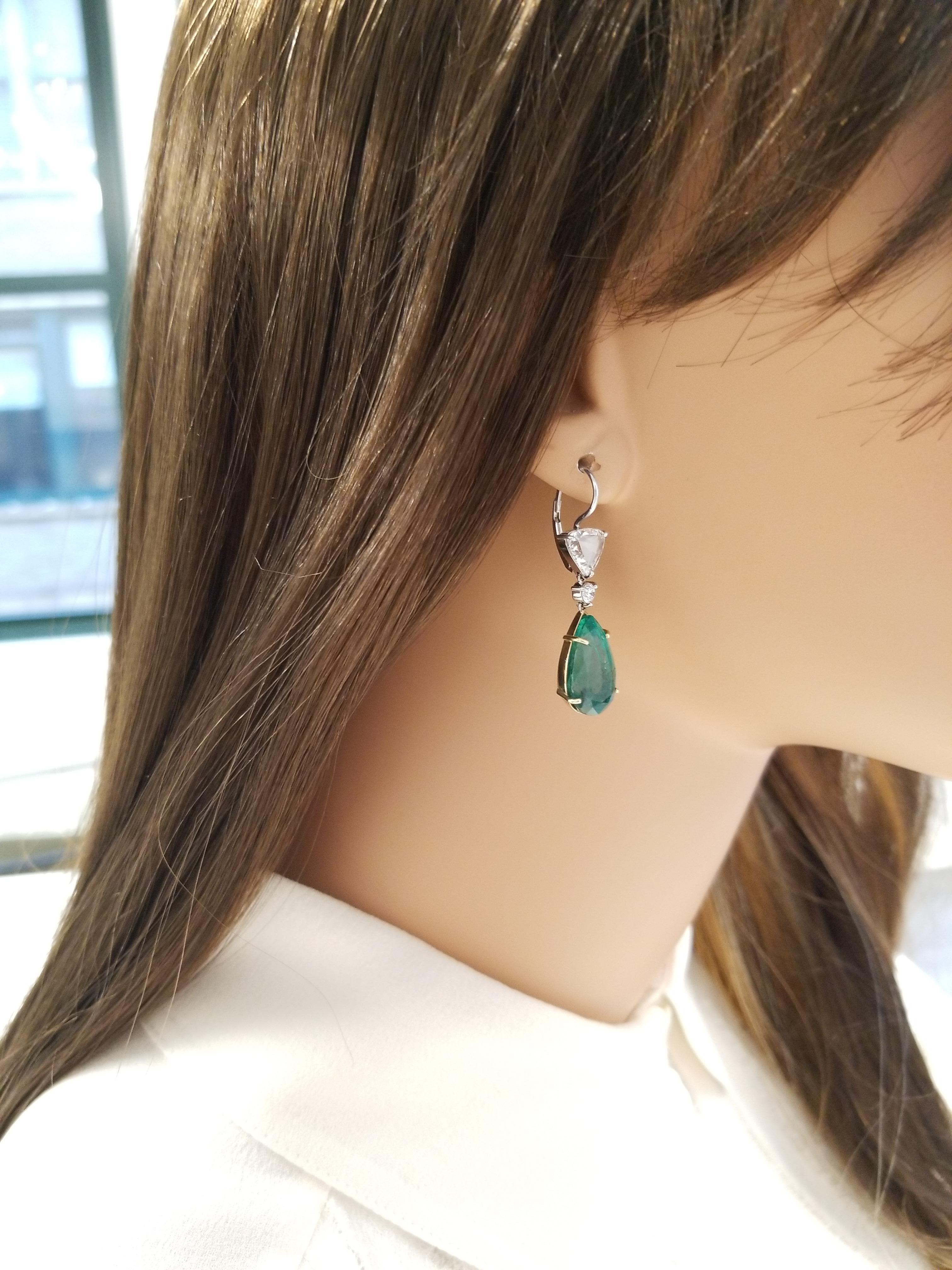 These dangle drop earrings feature two pear-shaped emeralds in a rich yellow gold prong setting totaling 14.11 carats that exhibit a vivid grass-green color and are accompanied by a PGS gem certification. Two triangular rose cut diamonds are prong