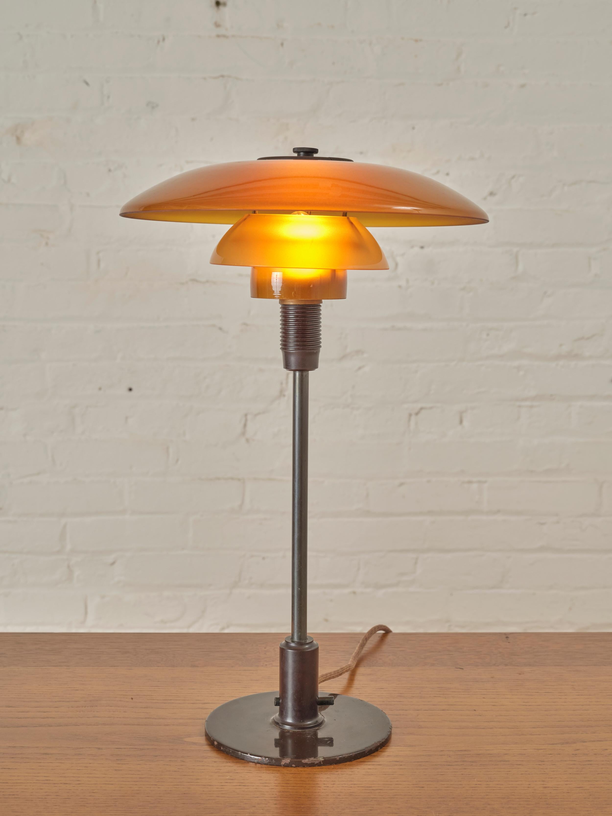 Table PH 4/3 de Poul Henningsen pour Louis Poulsen, présentant un système de lampe à 3 abat-jours en verre ambré soufflé à la main.

