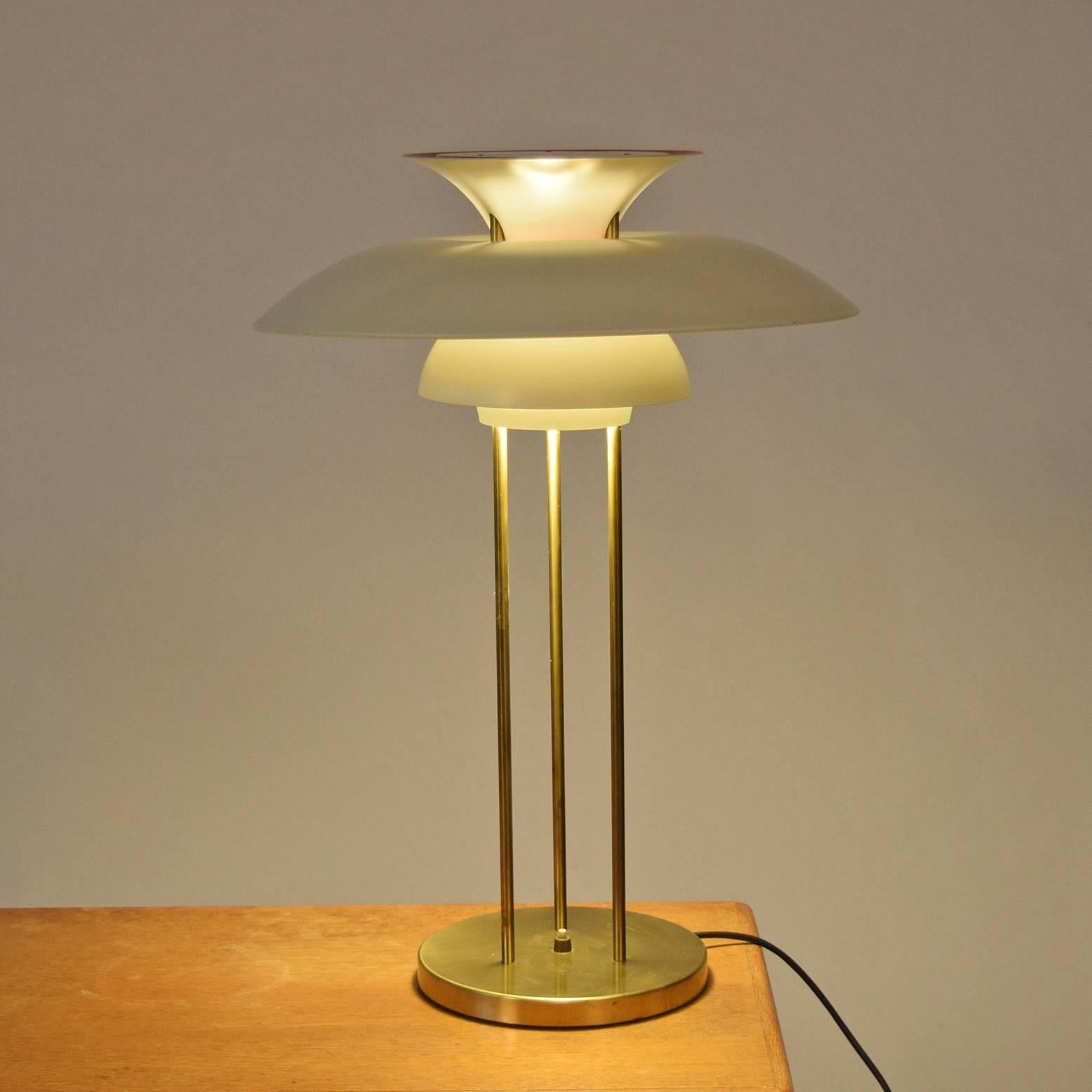 Table lamp with three brass legs on brass base with white painted metal shades, blue inner ring and red top. Taken out of production in the mid-1980s. Made by Louis Poulsen. Retains label.