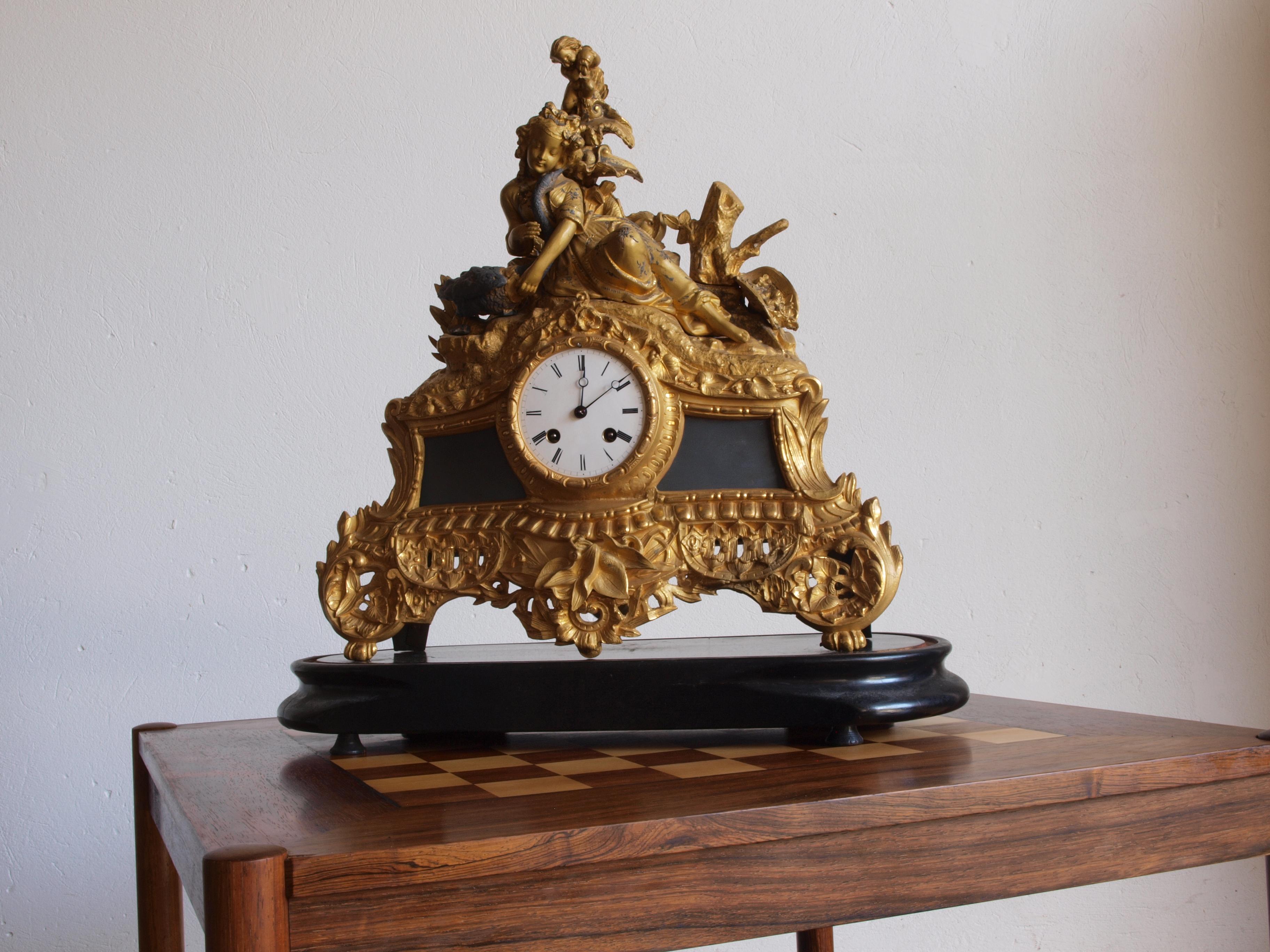This is a large late 19th-century gilt spelter mantle clock produced by Phillipe H. Mourey (1840-1910) in France. It features a female sculpture with a swan on top. The clock comes with a key, and the dome is intact, though the clock's functionality