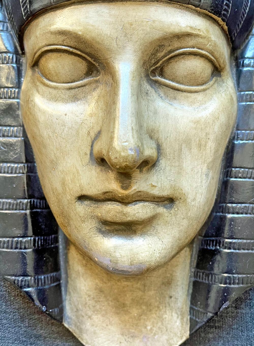 Beautifully sculpted and finished, this wall-mounted sculpture depicts the head of a Pharaoh, handsomely depicted with full lips and wide eyes, surmounted by a Classic Egyptian headdress with a winged scarab. The sculpture is molded plaster painted